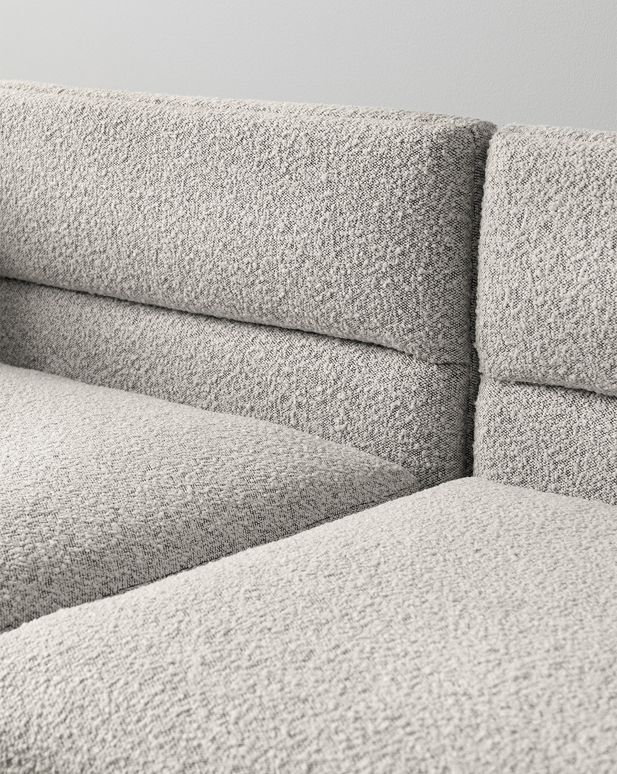 Close-up view of the Makerspalm Claremont Modular Sofa 99 in textured light gray fabric, featuring clean lines and a minimalist design against a plain light-colored wall. Vendixs