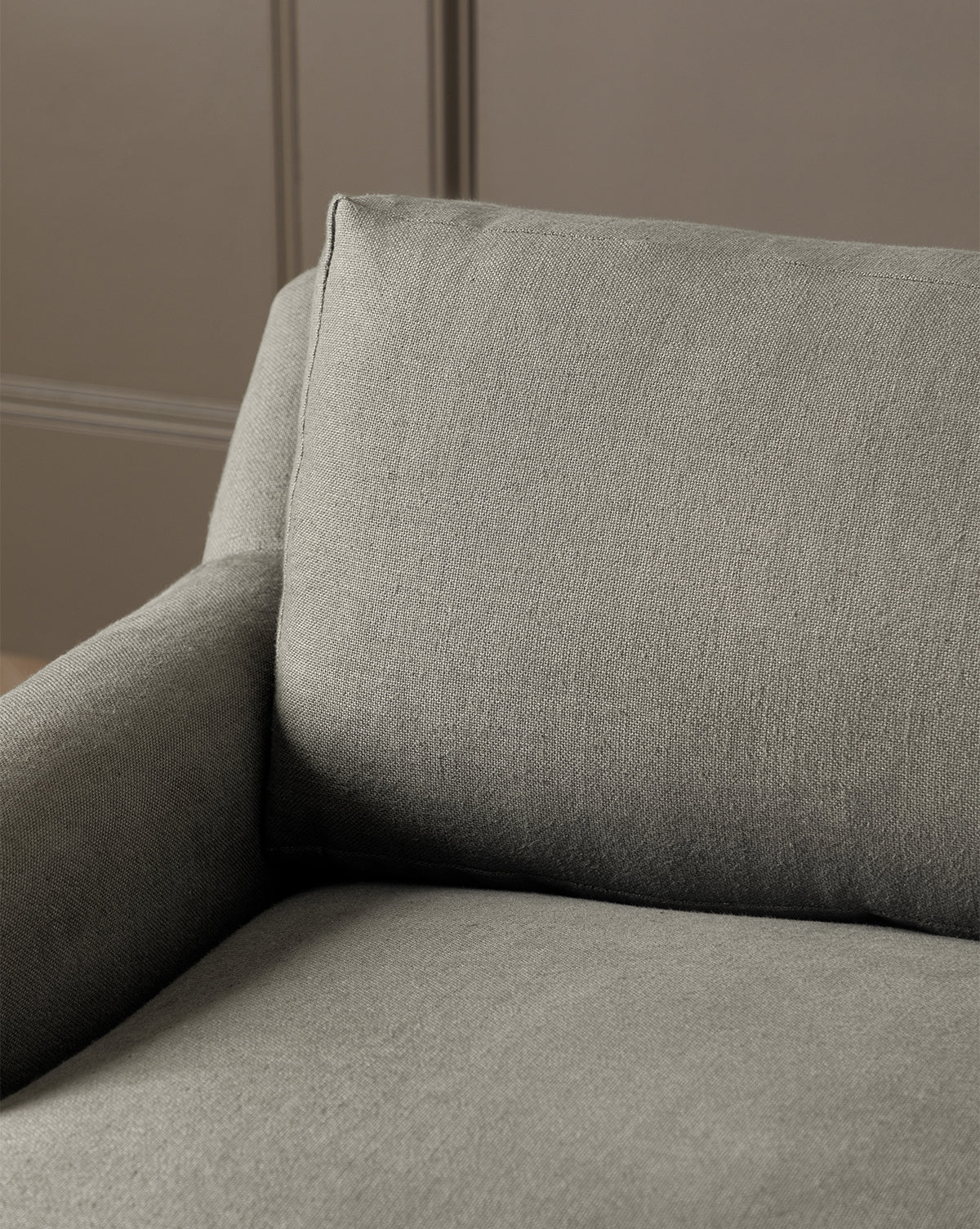Close-up of the Lucille English Roll Arm Chair and a Half, featuring gray upholstery, a cushioned down-wrapped seat, soft backrest and armrests, set against a plain beige paneled wall, by Vendixs
