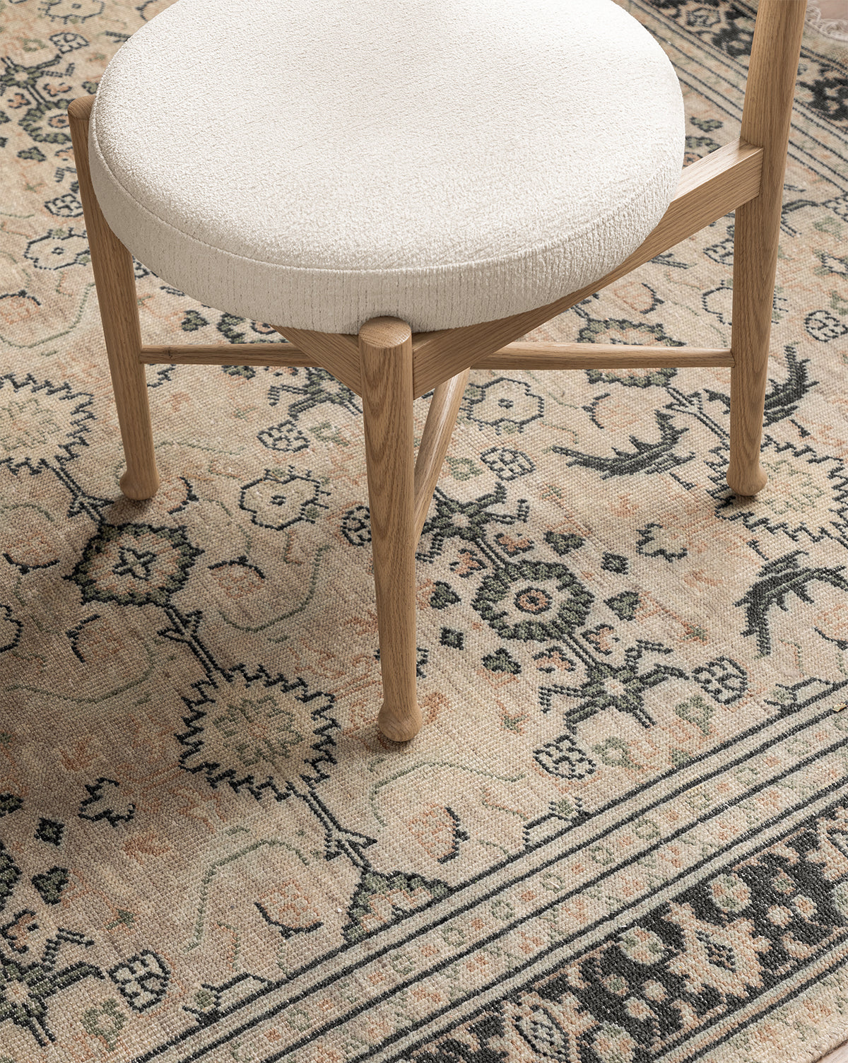 The Garance Dining Chair, featuring white oak and a round white cushioned seat, is placed on a beige and black rug with floral and geometric patterns, by Vendixs