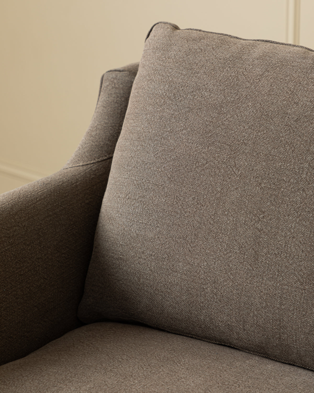 Close-up of the Haverford Upholstered Lounge Chair with a matching cushion, highlighting its brown fabric texture and soft padding, by McGee & Co. The background is softly blurred and features a light-colored wall.