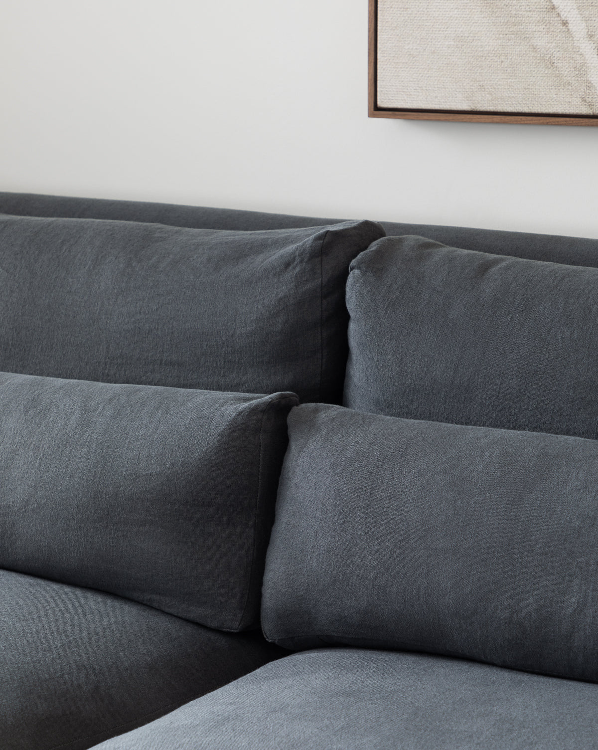 Close-up of the Beckstead Chaise Sectional by Community, featuring modern dark gray fabric and plush cushions, set against a light-colored wall with partially visible framed artwork above, Vendixs