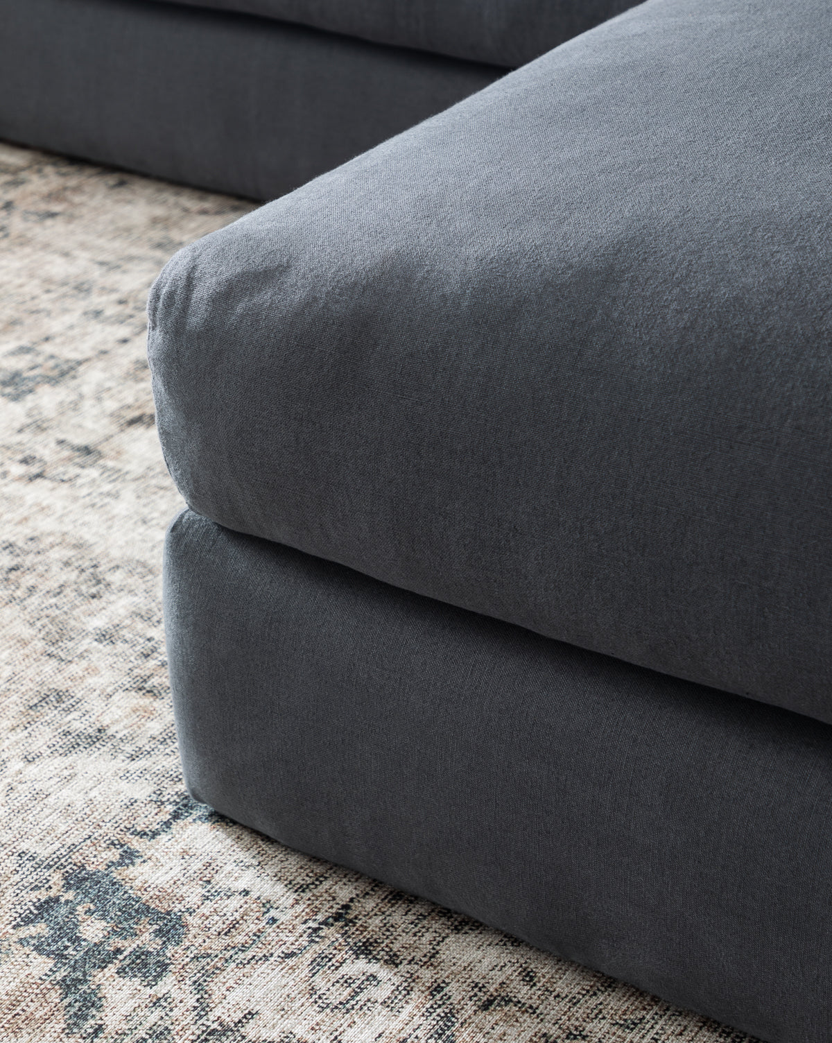 Close-up of a dark gray upholstered cushion from the Community Beckstead Chaise Sectional (Copy), set against a patterned neutral-toned area rug, Vendixs