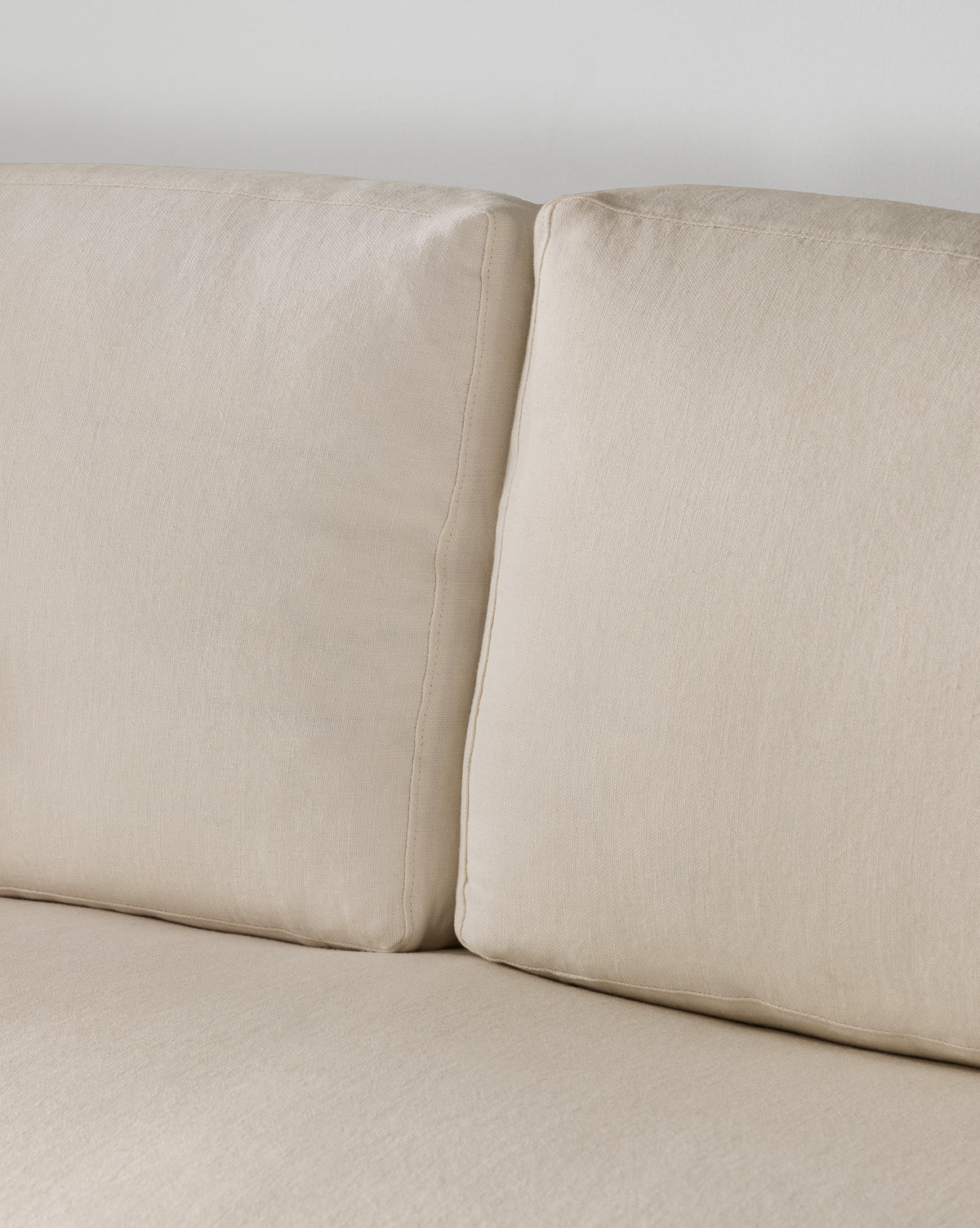 Close-up of two beige sofa cushions with a visible seam, set against a light wall. These soft, textured cushions are part of the Community Macy Slipcover Chaise Sectional 101 by Vendixs