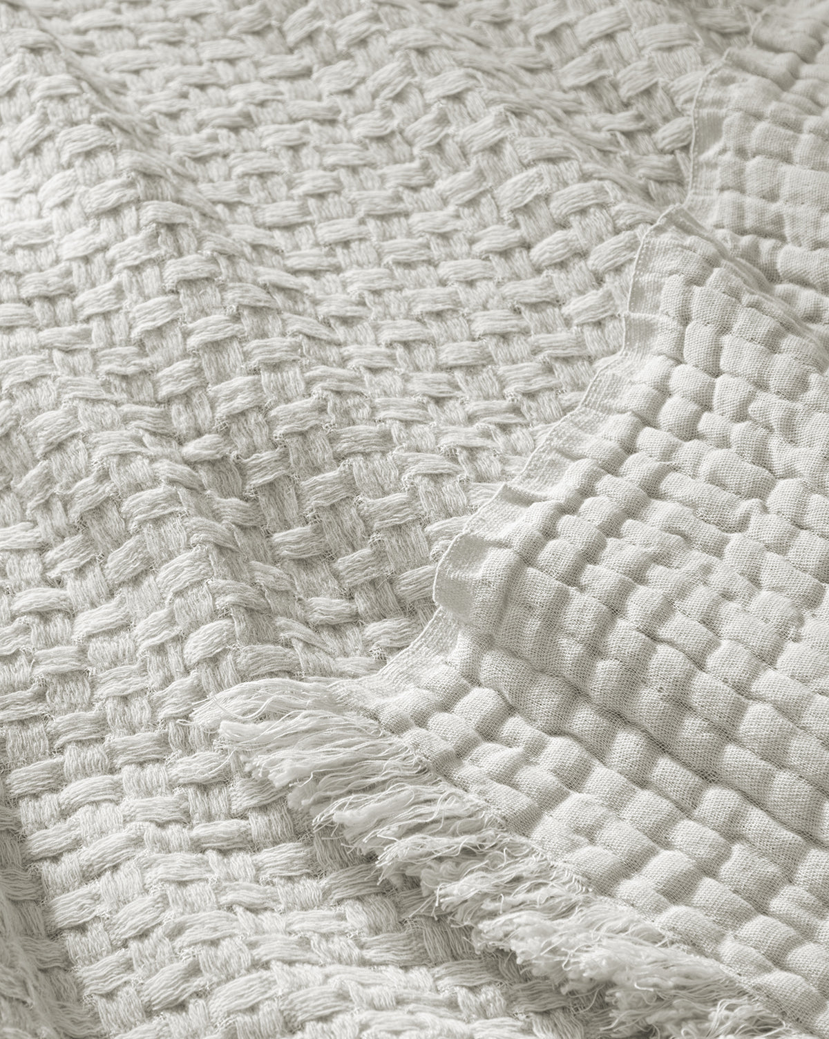 A close-up of two off-white Caroline Kids Blankets by Indigo Craft—one shows a thick basket weave, the other a finer grid pattern with frayed edges, both resembling soft woven textures. Vendixs