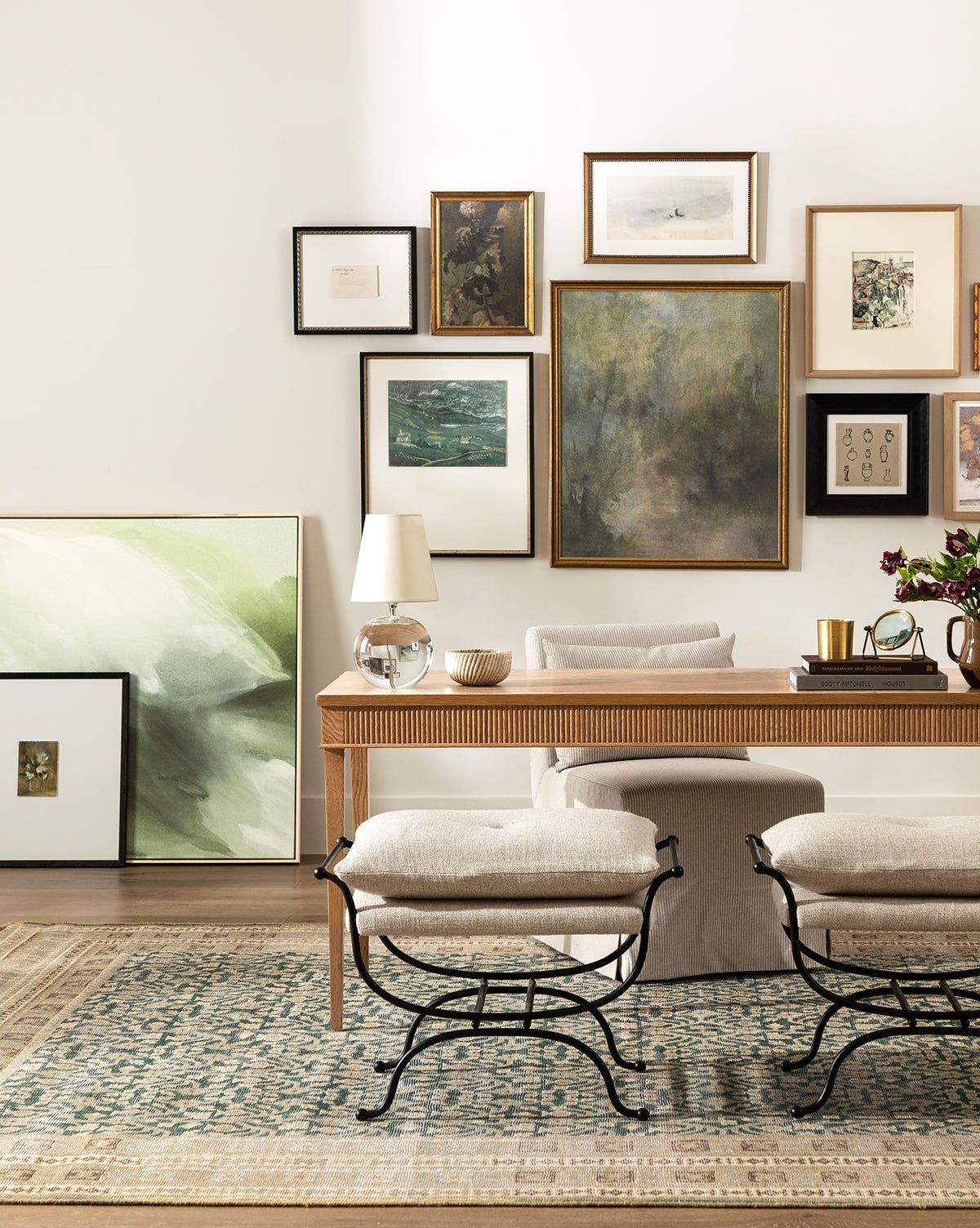 A stylish home office with a wood desk, neutral chair, two stools, a green-patterned rug, and the Fields of Green canvas art featured above the desk. Abstract art completes the gallery wall, while a table lamp and decor add finishing touches, by Vendixs
