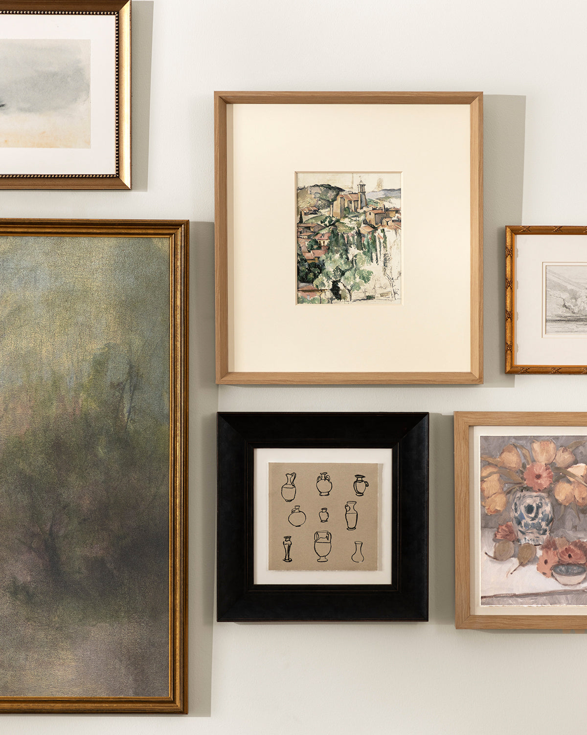 A gallery wall with five Le Village framed artworks, featuring museum-quality giclee prints of landscapes, vases, and scenes arranged as a collage on a light-colored wall in natural woodgrain frames by Vendixs