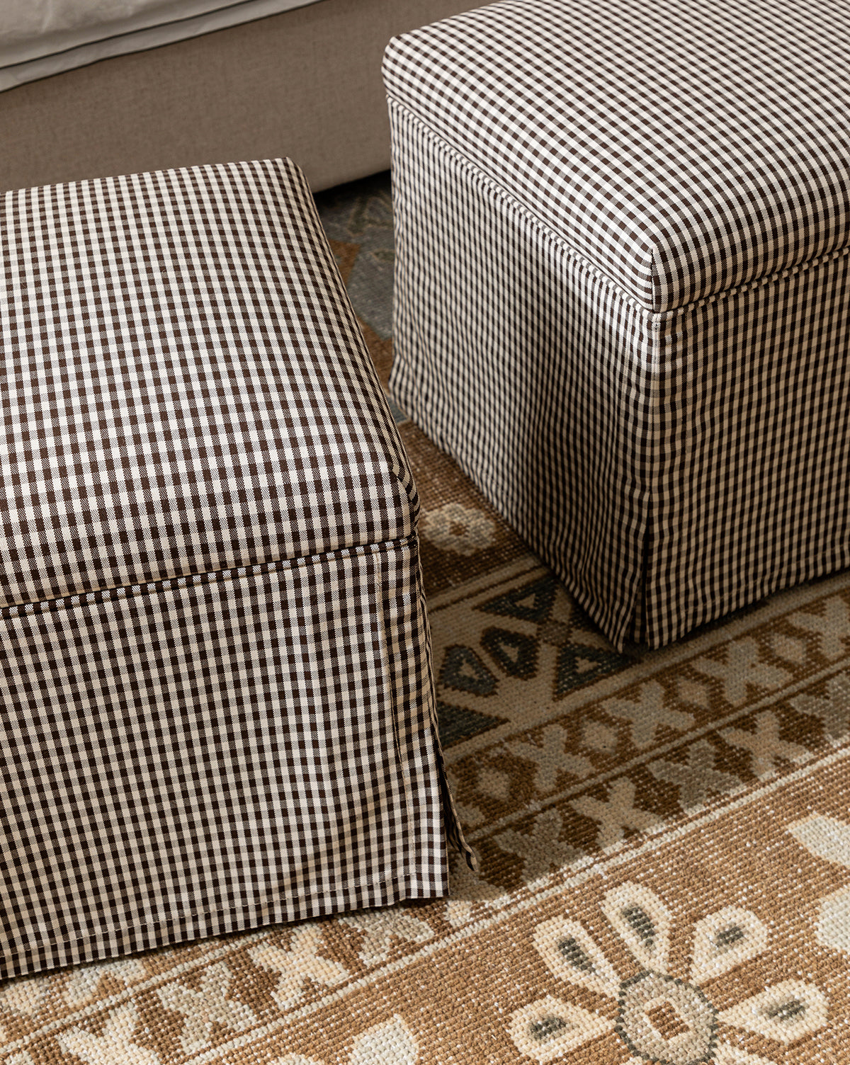 Two Makerspalm Latimer Ottomans (Ready to Ship) with black and white gingham fabric rest on a patterned beige and brown rug next to a light sofa, offering stylish, functional accent seating by Vendixs