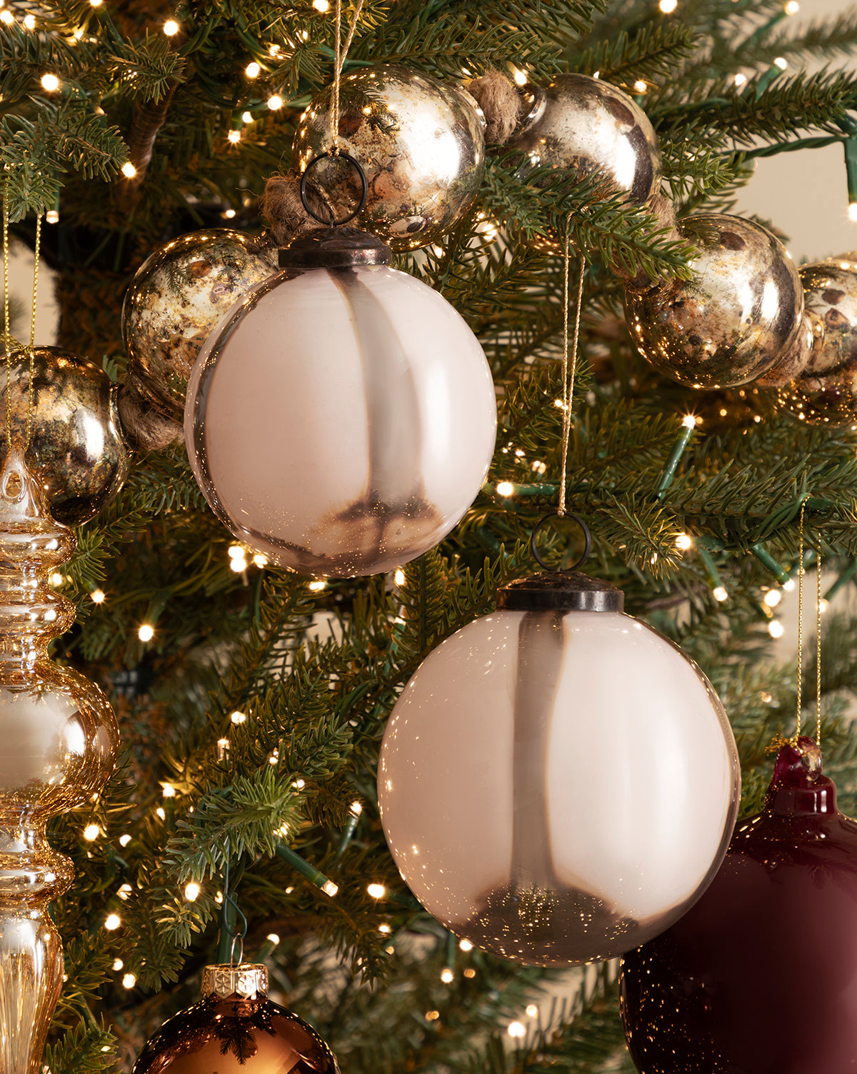 A 4" Striped Glass Bauble hangs on the holiday tree, aglow with white string lights and surrounded by gold and burgundy ornaments amid green pine needles, by Vendixs