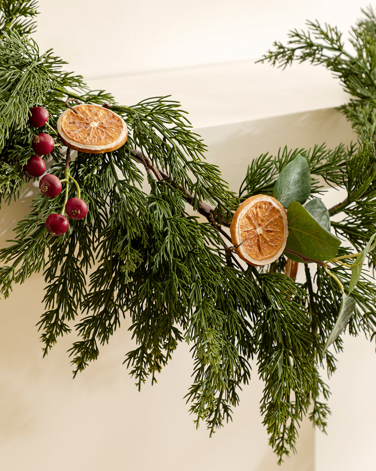 The 6' Orange & Eucalyptus Faux Garland, featuring lifelike pine branches, dried orange slices, red berries, and green leaves, adds festive charm to any corner or white surface for seasonal decor, by Vendixs