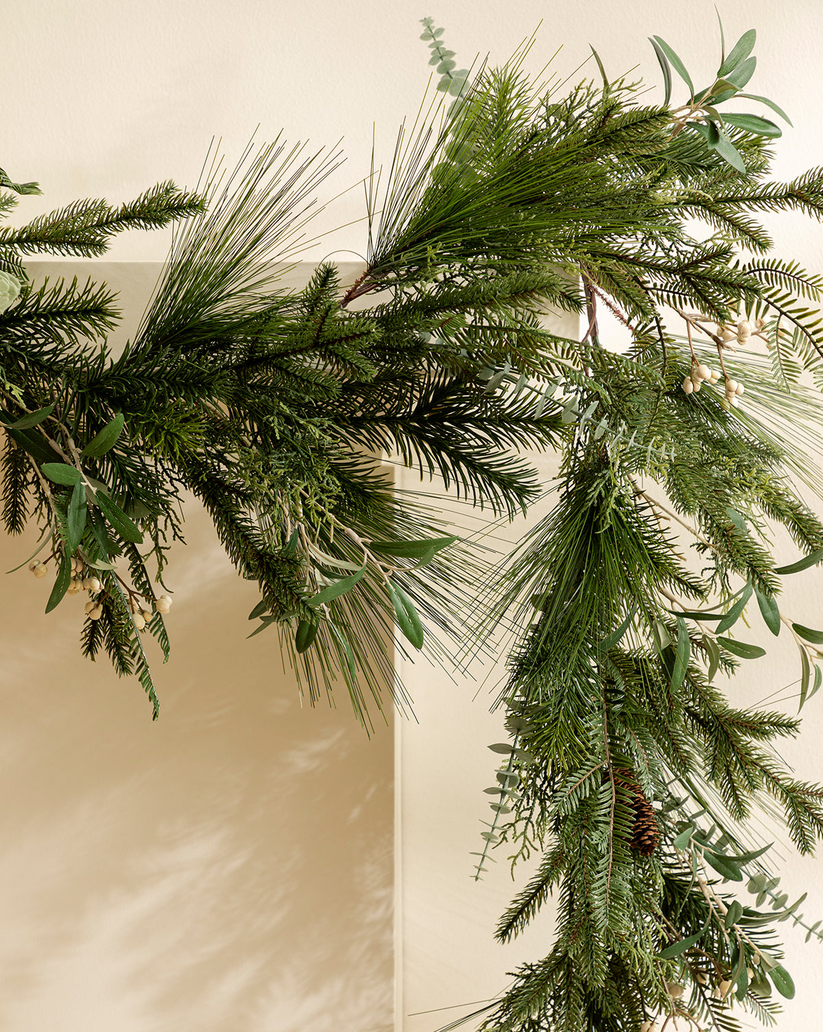 A close-up of the 6' Pinecone & Berries Faux Garland draped over a light wall, showcasing lifelike foliage, pine cones, and berries—ideal for enhancing your holiday décor with a touch of nature, by Vendixs