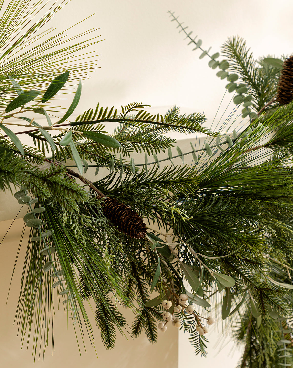 The 6' Pinecone & Berries Faux Garland features festive pine branches and red berries, ideal for bringing holiday charm to your space when draped along a light-colored wall, by Vendixs