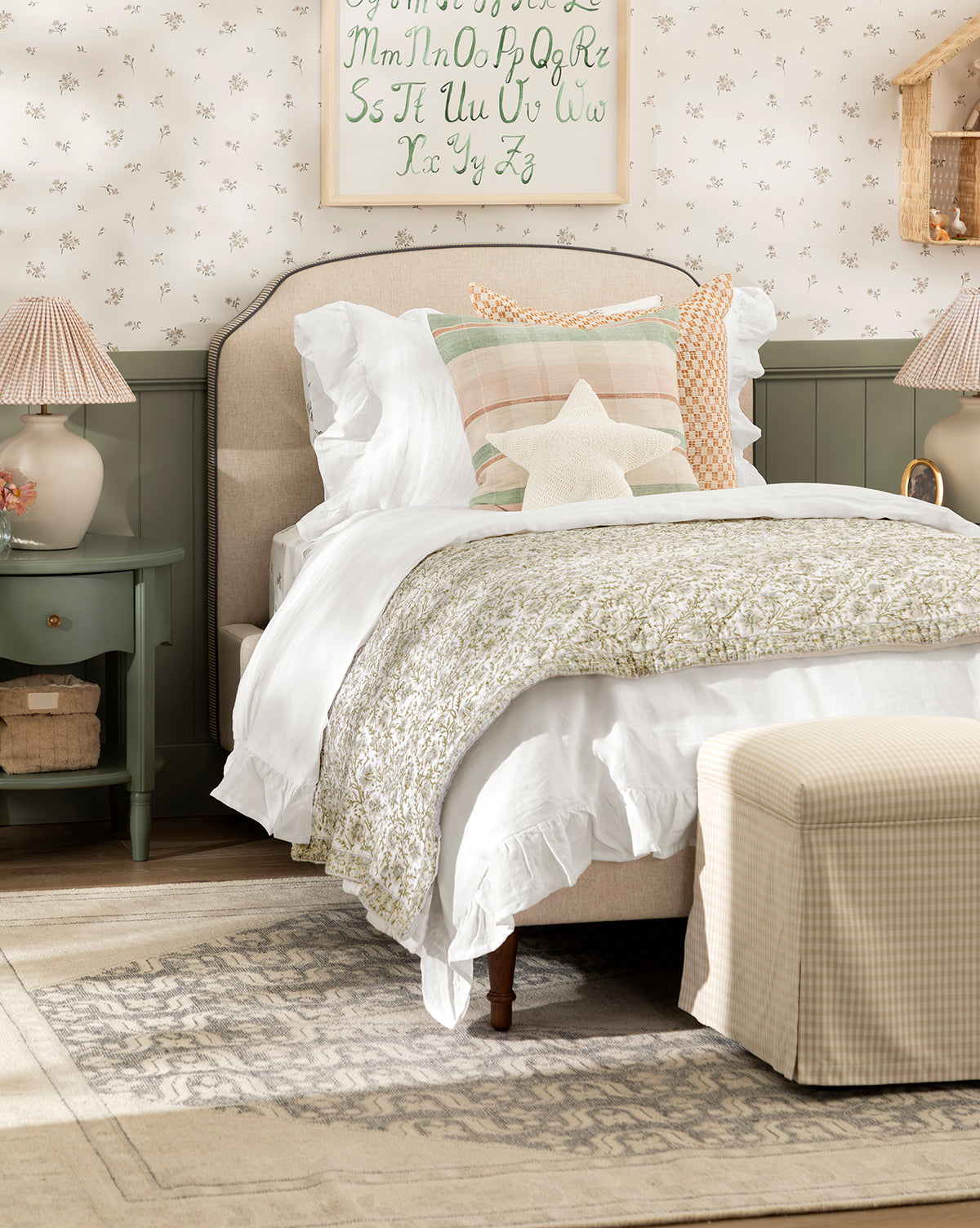 Cozy bedroom with a soft bed featuring the Seton Kids Quilt, white ruffled bedding, pastel pillows, a star cushion, green nightstand, matching lamps, floral wallpaper, and a decorative alphabet print above the headboard, by Vendixs