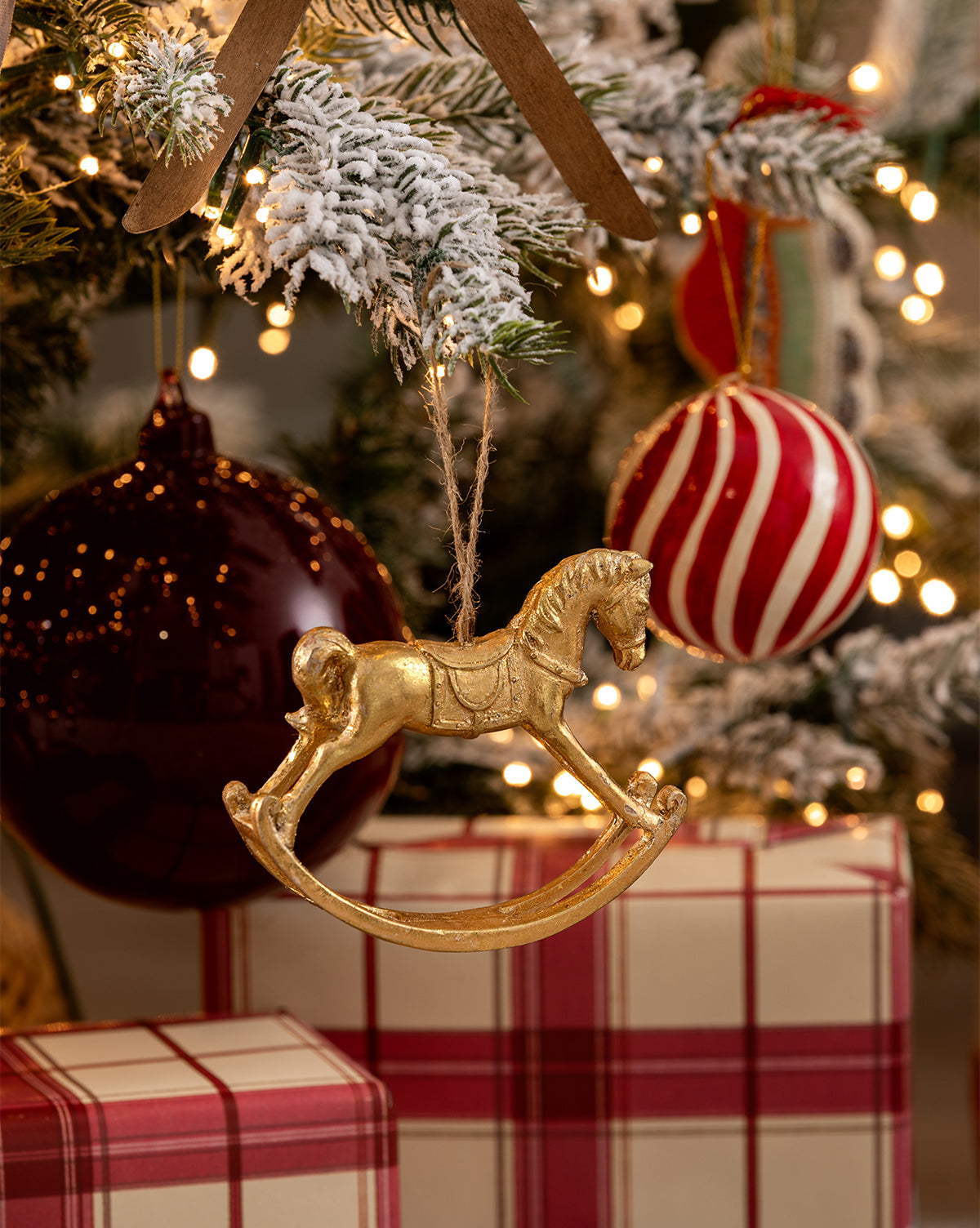 A Magical Wonderland Tree decorated with lights, gingerbread ornaments, a gold rocking horse ornament, a red-and-white striped ornament, and presents in red plaid paper underneath, by Vendixs
