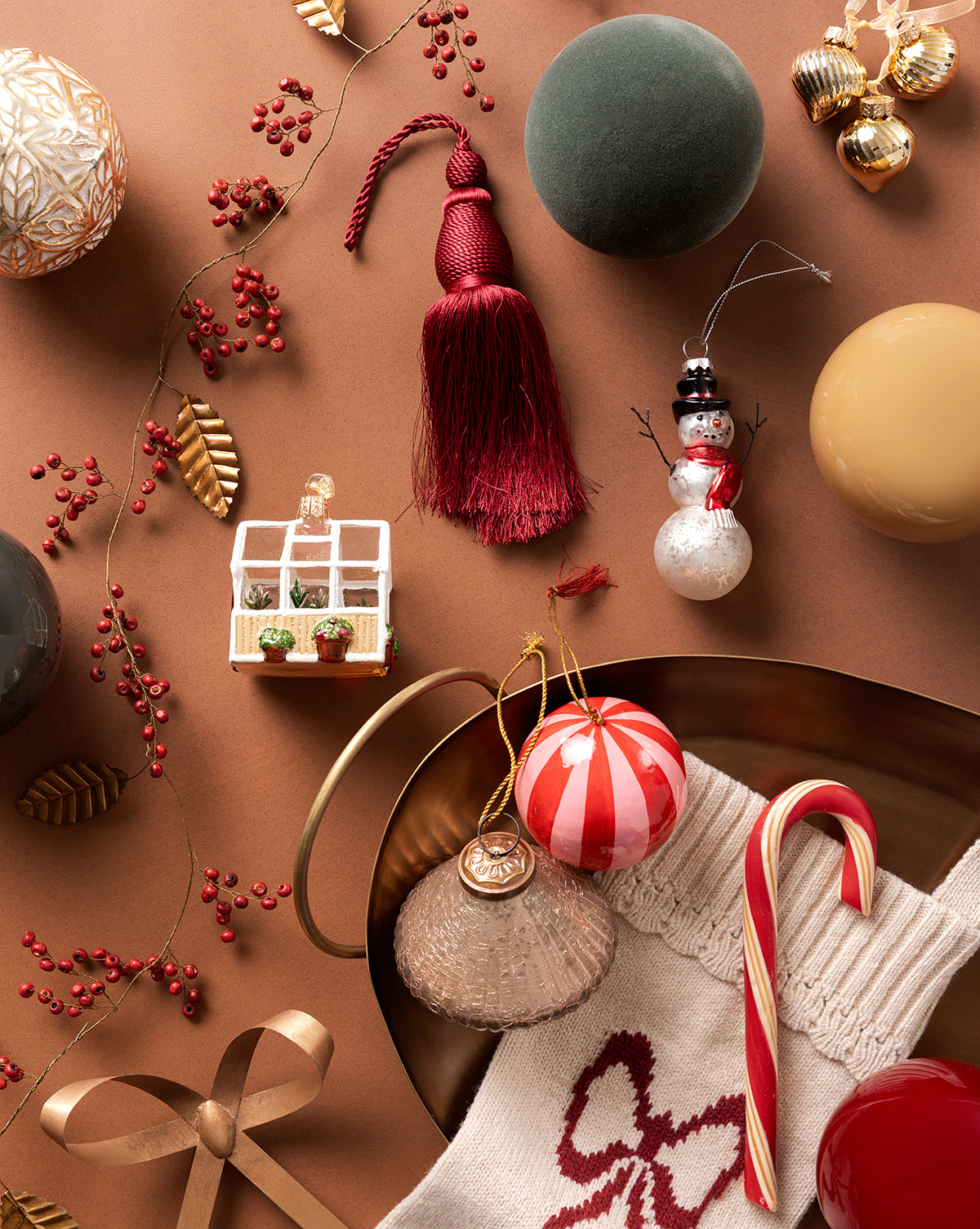 A festive flatlay with holiday ornaments, a red tassel, candy cane, knit stocking, gold ribbon, faux berries, and a red-and-white bauble from the 4" Assorted Flocked Baubles (Set of 4), all on a brown background, by Vendixs