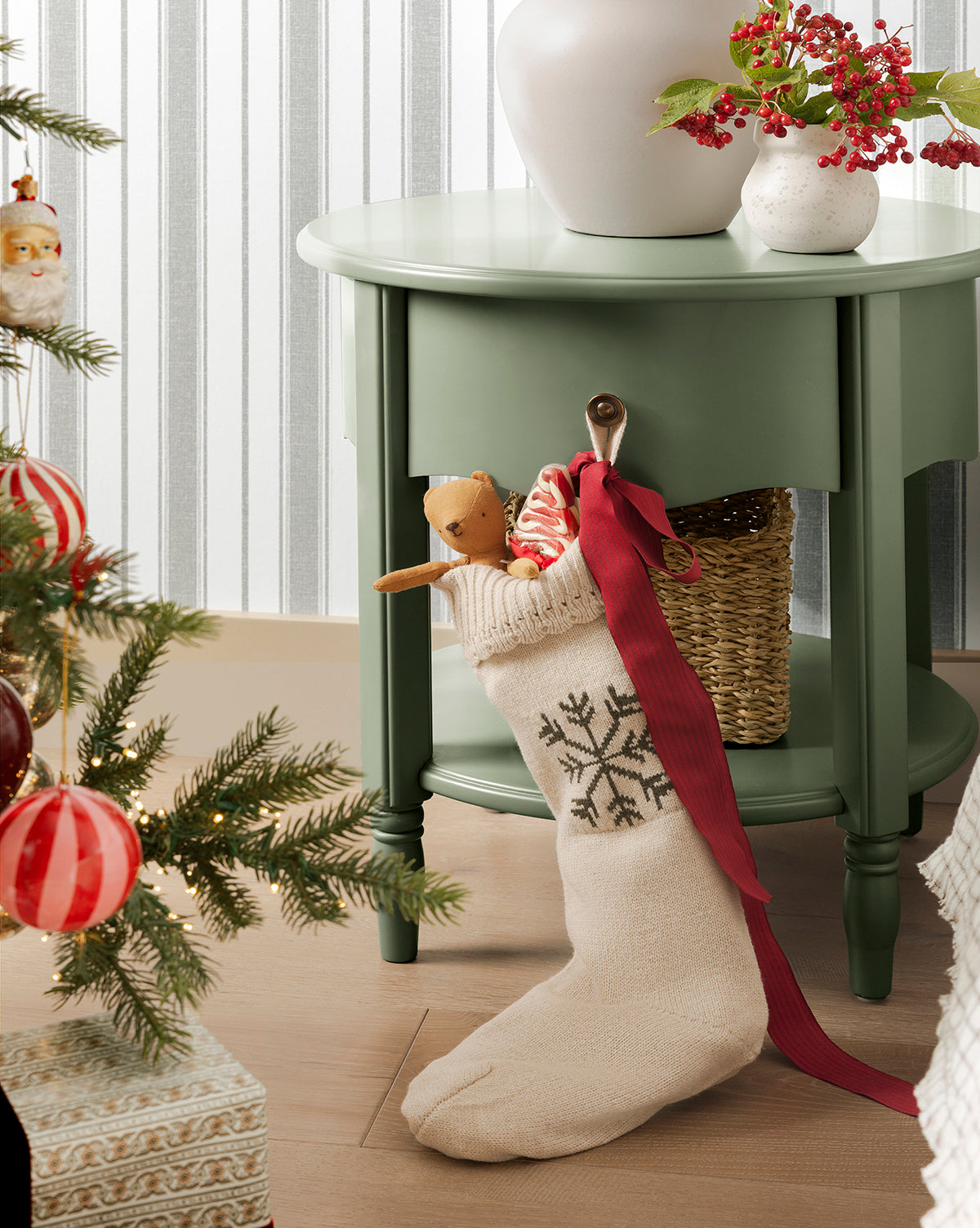A cream-colored Bella Scalloped Stocking with Snowflake hangs on a green side table, filled with gifts and a reindeer plush, surrounded by festive holiday mantel decor, by Vendixs