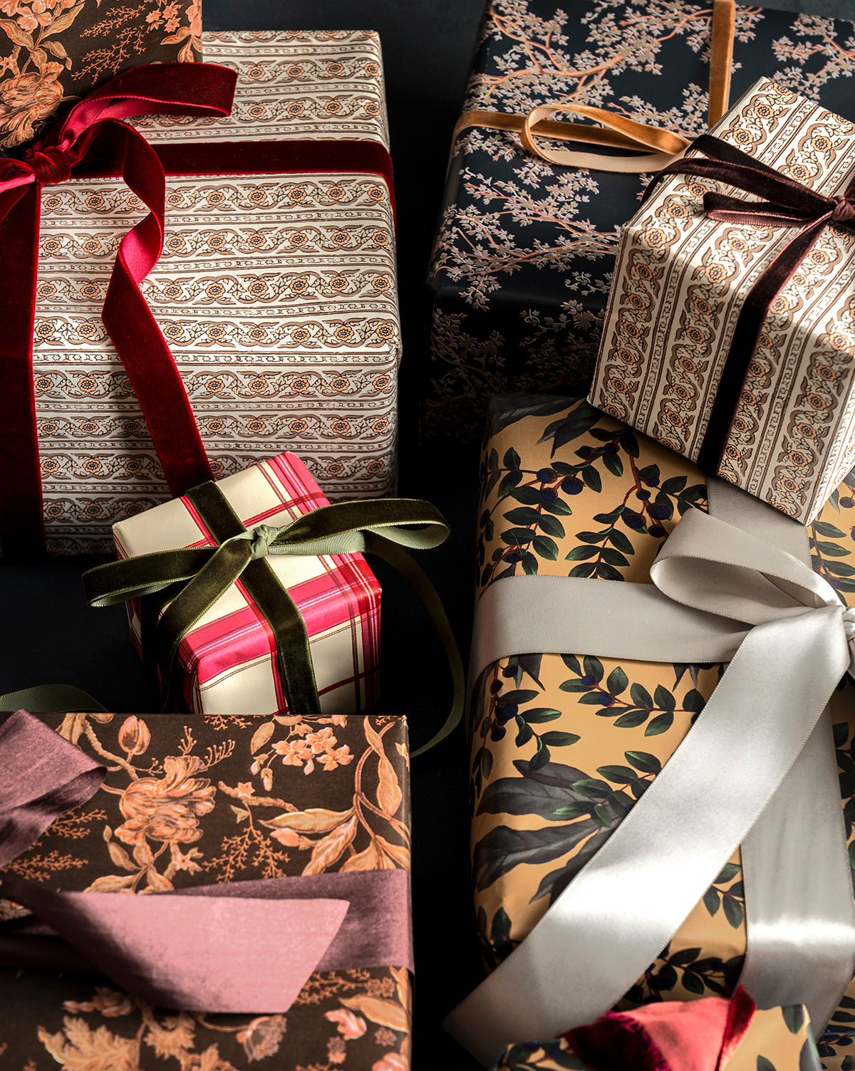 A set of Foragers Gift Wrap presents, beautifully wrapped in floral, striped, and leafy designs with colorful ribbons, arranged closely together against a dark background, by Vendixs
