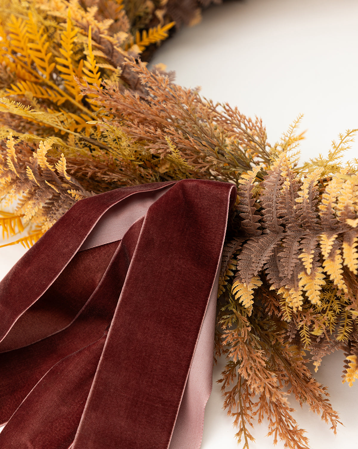 A close-up of the 30 Faux Golden Fern Wreath, featuring yellow and brown faux ferns with a dark red velvet ribbon, perfect for fall entryway decor against a white background, by Vendixs