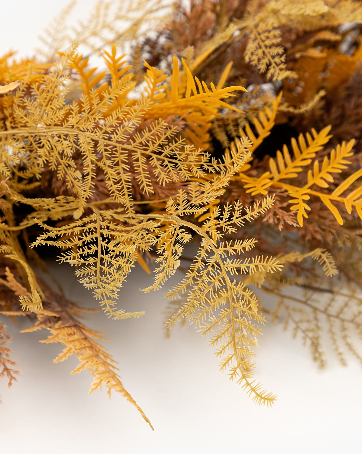 Close-up of delicate yellow and brown dried fern leaves on a white background, echoing the fine textures of a 30 Faux Golden Fern Wreath—an elegant piece ideal for enhancing your entryway decor, by Vendixs