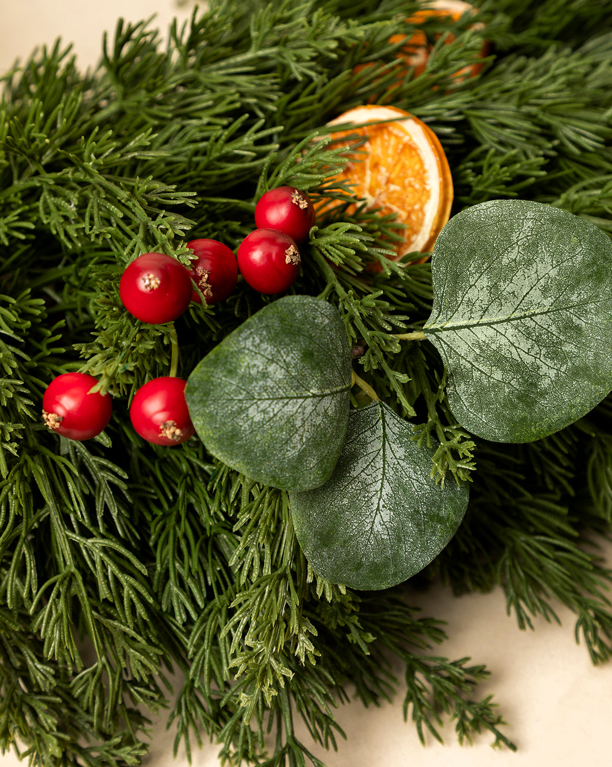 A close-up of a festive 30" Orange & Eucalyptus Faux Wreath, featuring pine branches, red berries, dried orange slices, and dark green eucalyptus leaves, by Vendixs