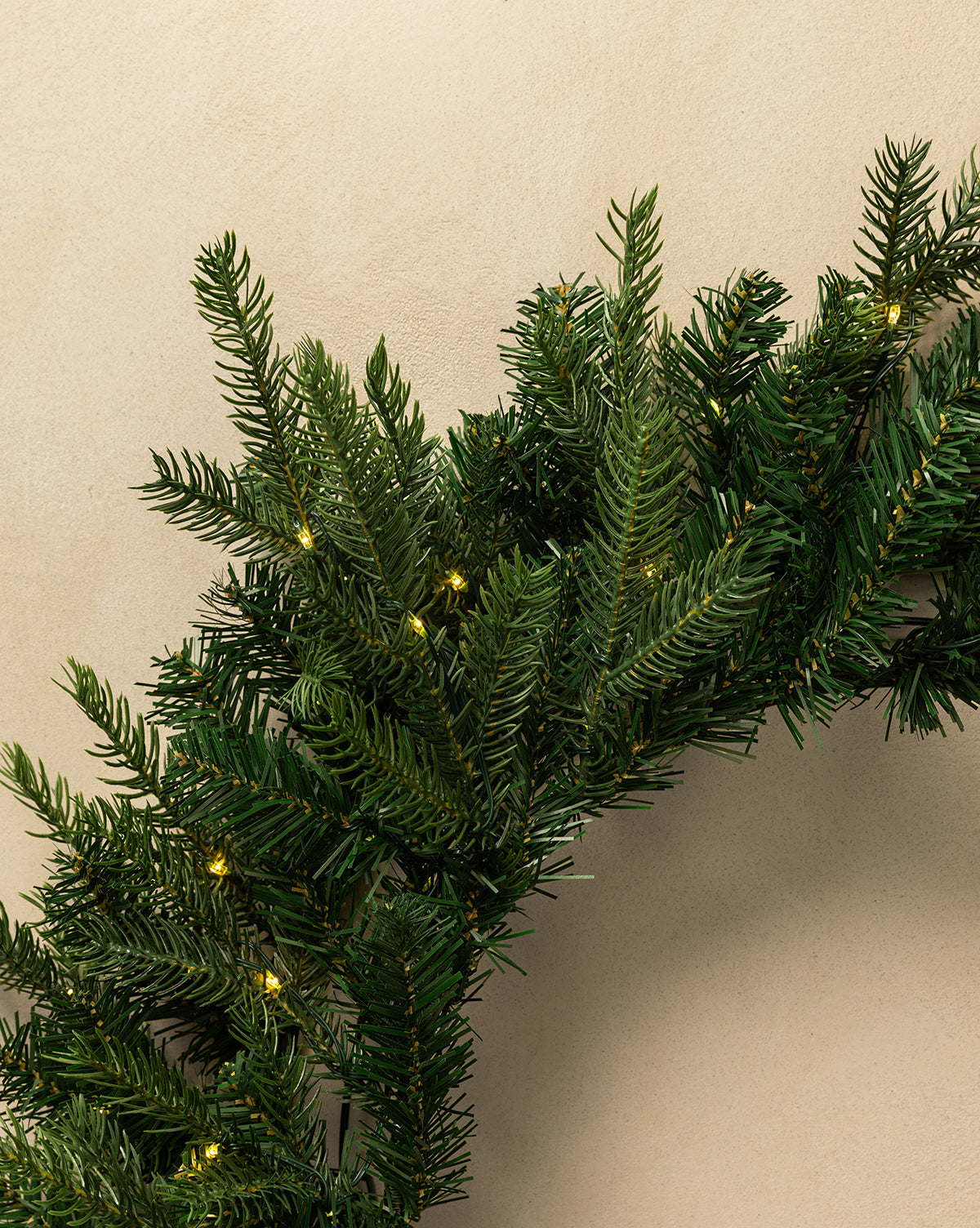 A close-up of the 32" Grandis Pre-Lit Indoor/Outdoor Faux Wreath, featuring lush greenery and warm white lights—perfect for holiday decorating against a beige backdrop, by Vendixs