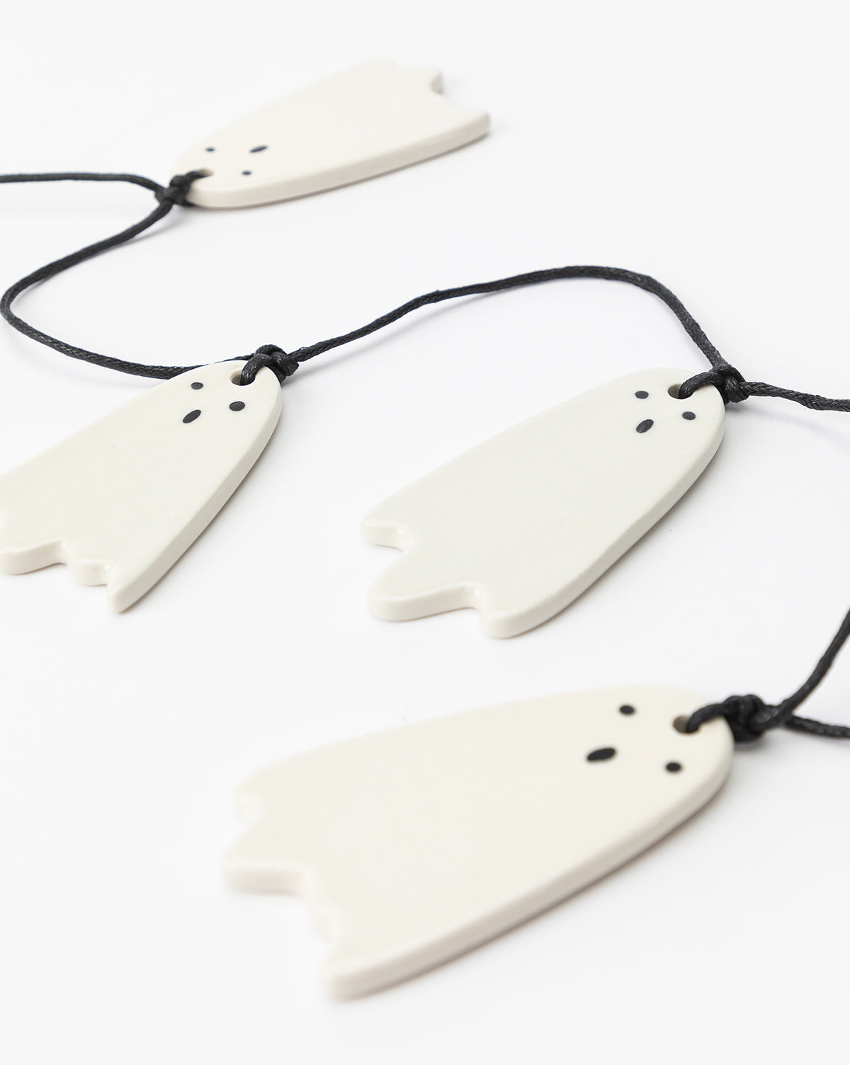 The 3 Ceramic Ghost Garland features four white ceramic ghosts with hand-detailed faces and black eyes and mouths, hanging on black strings—perfect for adding charm to your Halloween decor, by Vendixs