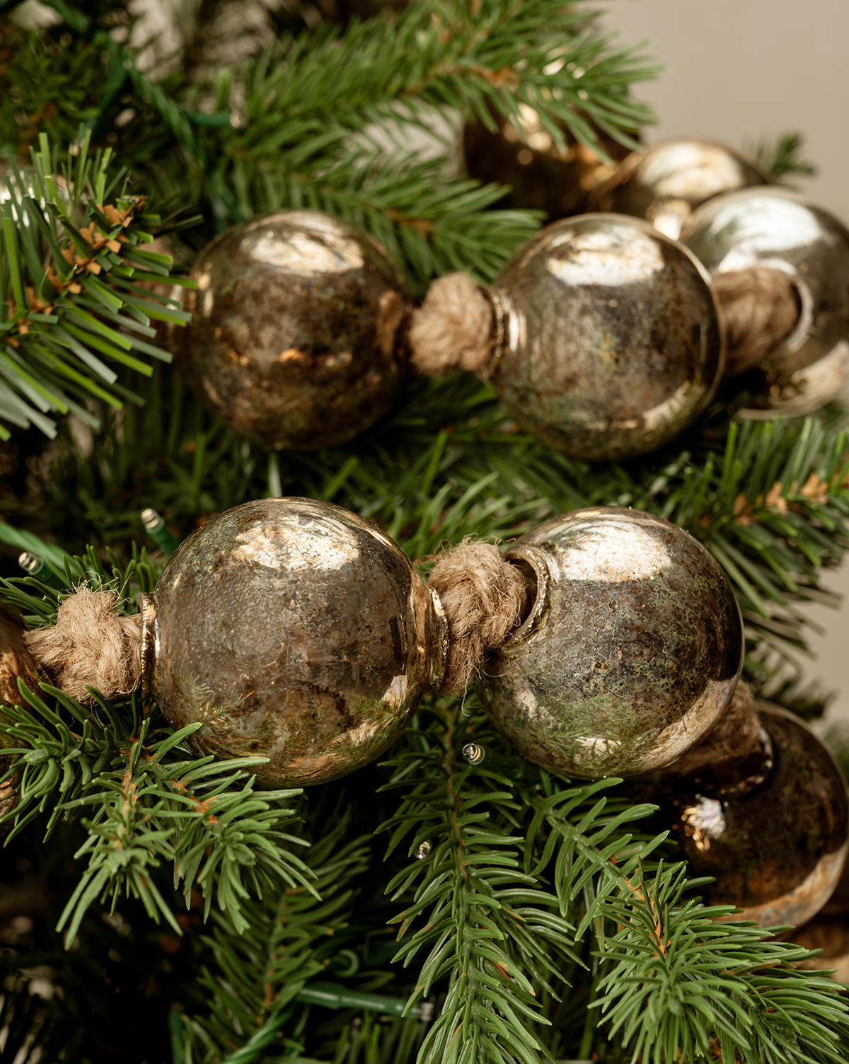 Close-up of vintage holiday decor with the 4.4' Aged Silver Glass Garland and silver beads, strung with twine and draped on pine tree branches, by Vendixs