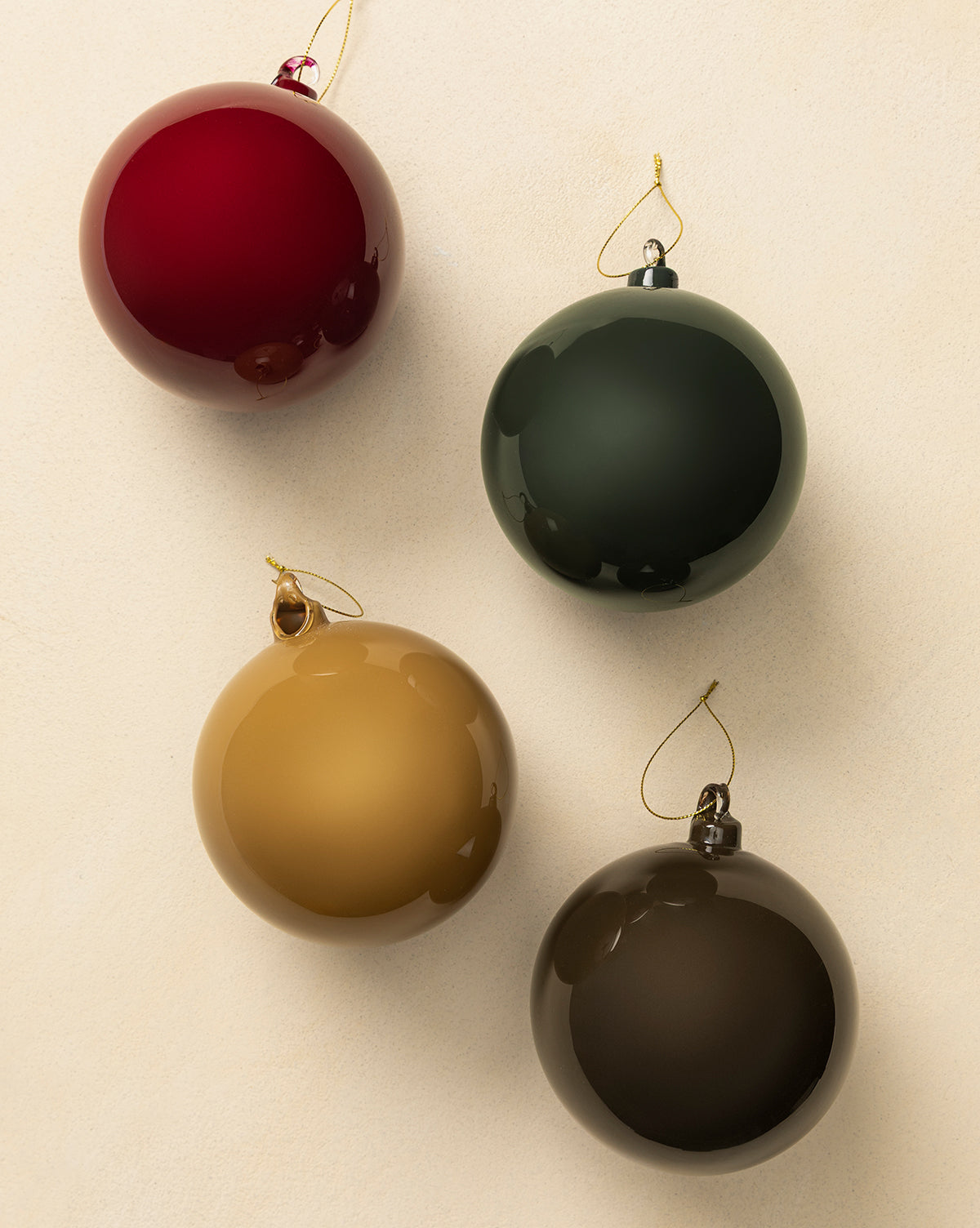 The 5" High Gloss Glass Baubles (Set of 4) in red, dark green, gold, and brown are arranged on a light beige surface. Each features a gold hanging string, making them perfect for holiday decorating, by Vendixs