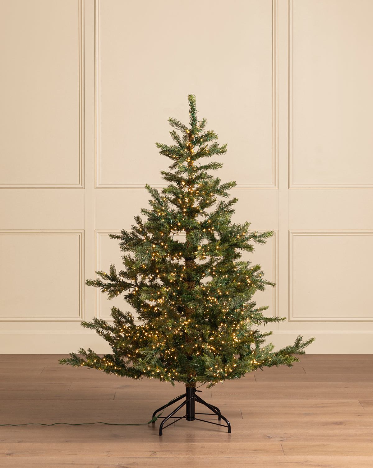 A 5' Grandis Fir Pre-Lit Faux Tree with warm white lights stands on a wooden floor against a cream paneled wall. The undecorated Christmas tree features an exposed metal stand, by Vendixs