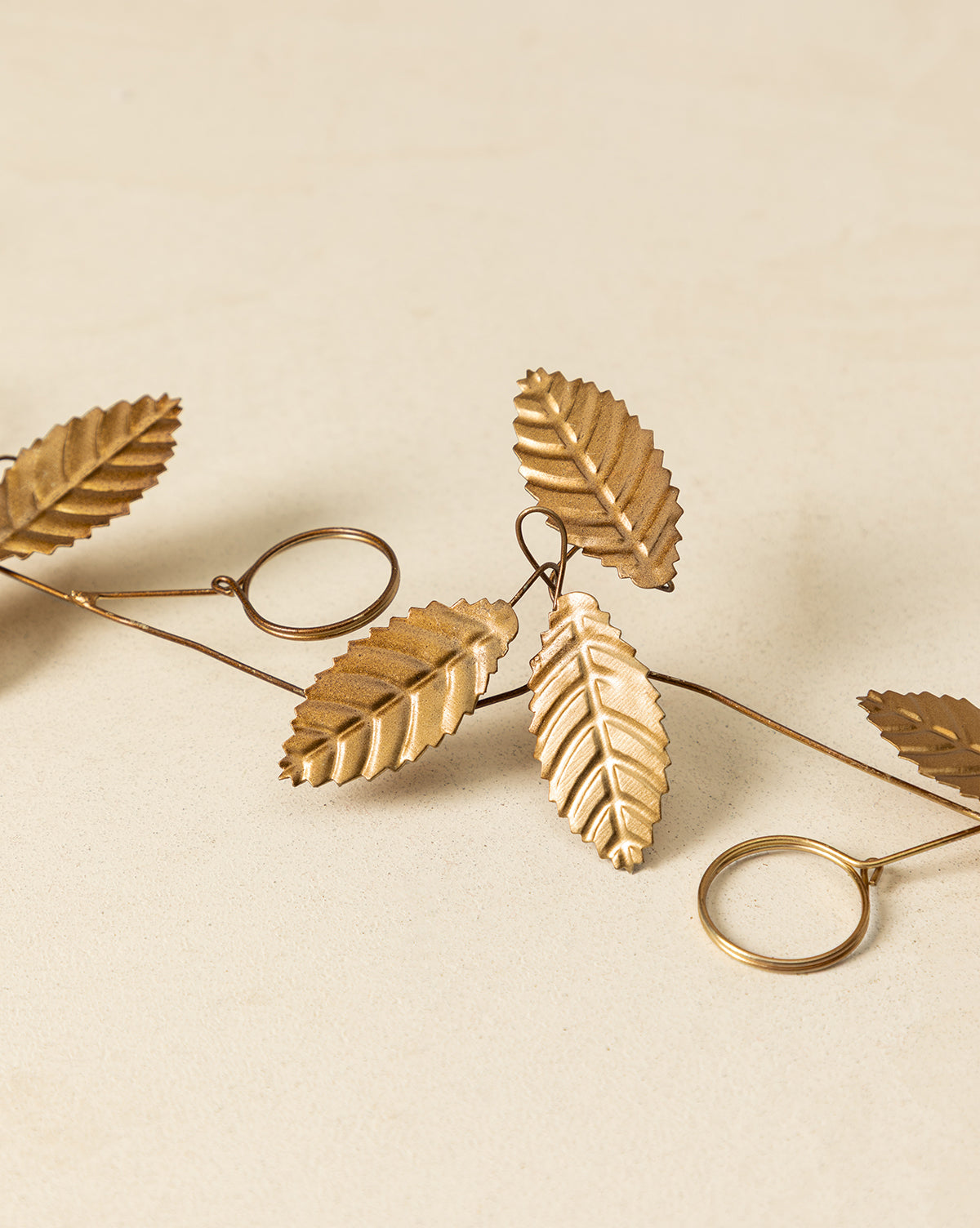 The 6' Card Holder Garland is a decorative gold-toned metal accent with detailed leaf shapes and circular rings, ideal as vintage-inspired decor or a unique holiday card display on a light beige background, by Vendixs