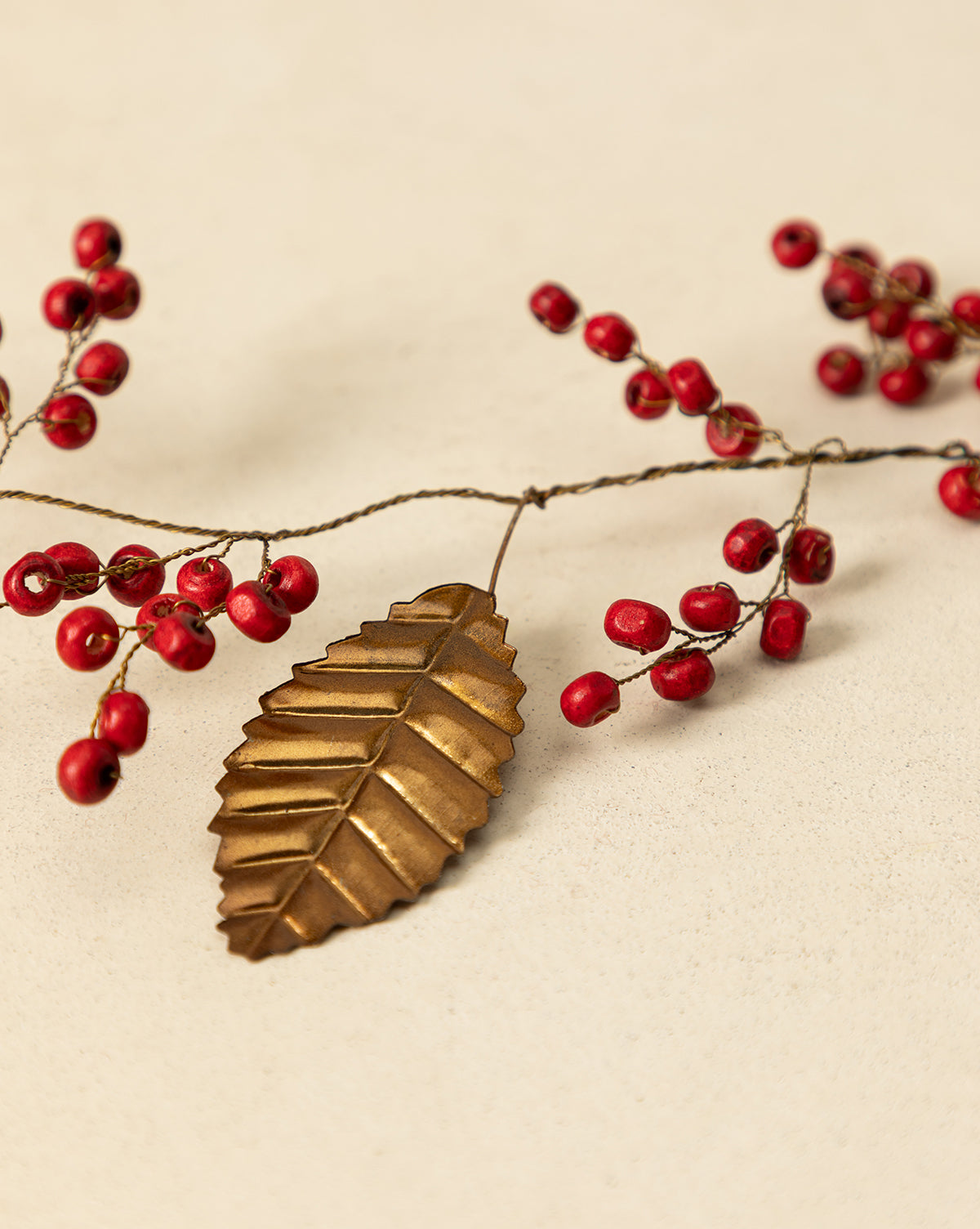 The 6' Holly Berry Garland, featuring metallic gold leaves and red berry sprigs, creates a simple yet elegant festive décor, perfect as a holiday accent on any light beige surface, by Vendixs