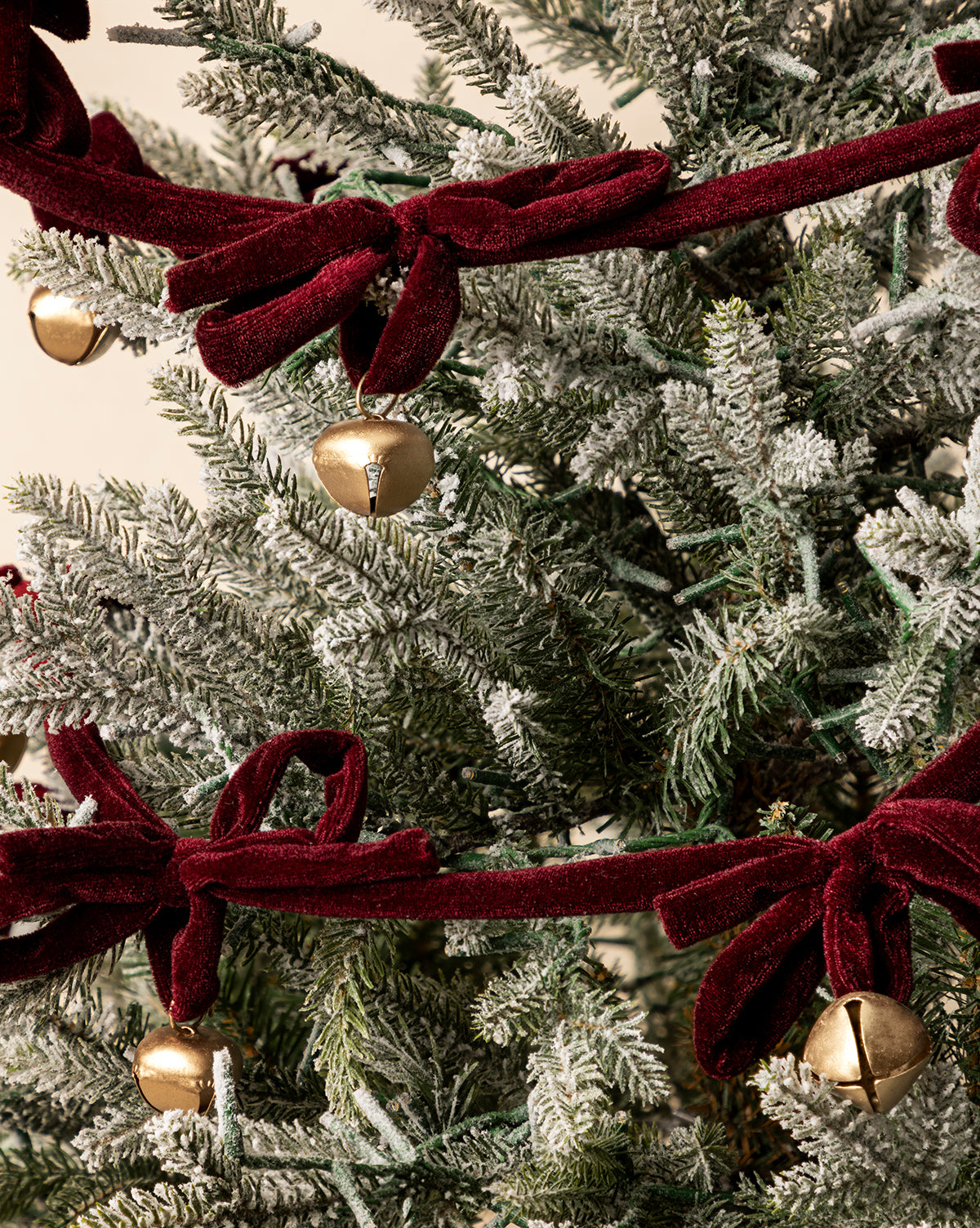 A close-up of the 6' Mini Bows & Bells Garland, showcasing velvet bows, gold jingle bells, and snow-dusted branches for festive holiday decor, by Vendixs