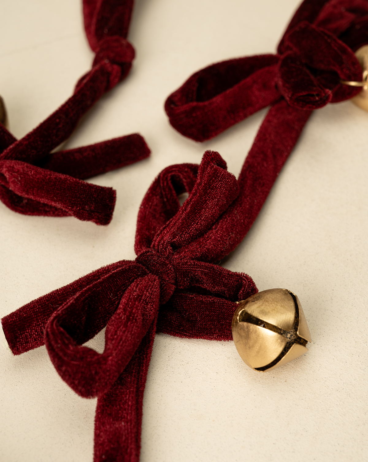 A close-up of the 6' Mini Bows & Bells Garland, featuring deep red velvet bows and small gold jingle bells on a light beige surface—ideal for festive holiday decor, by Vendixs
