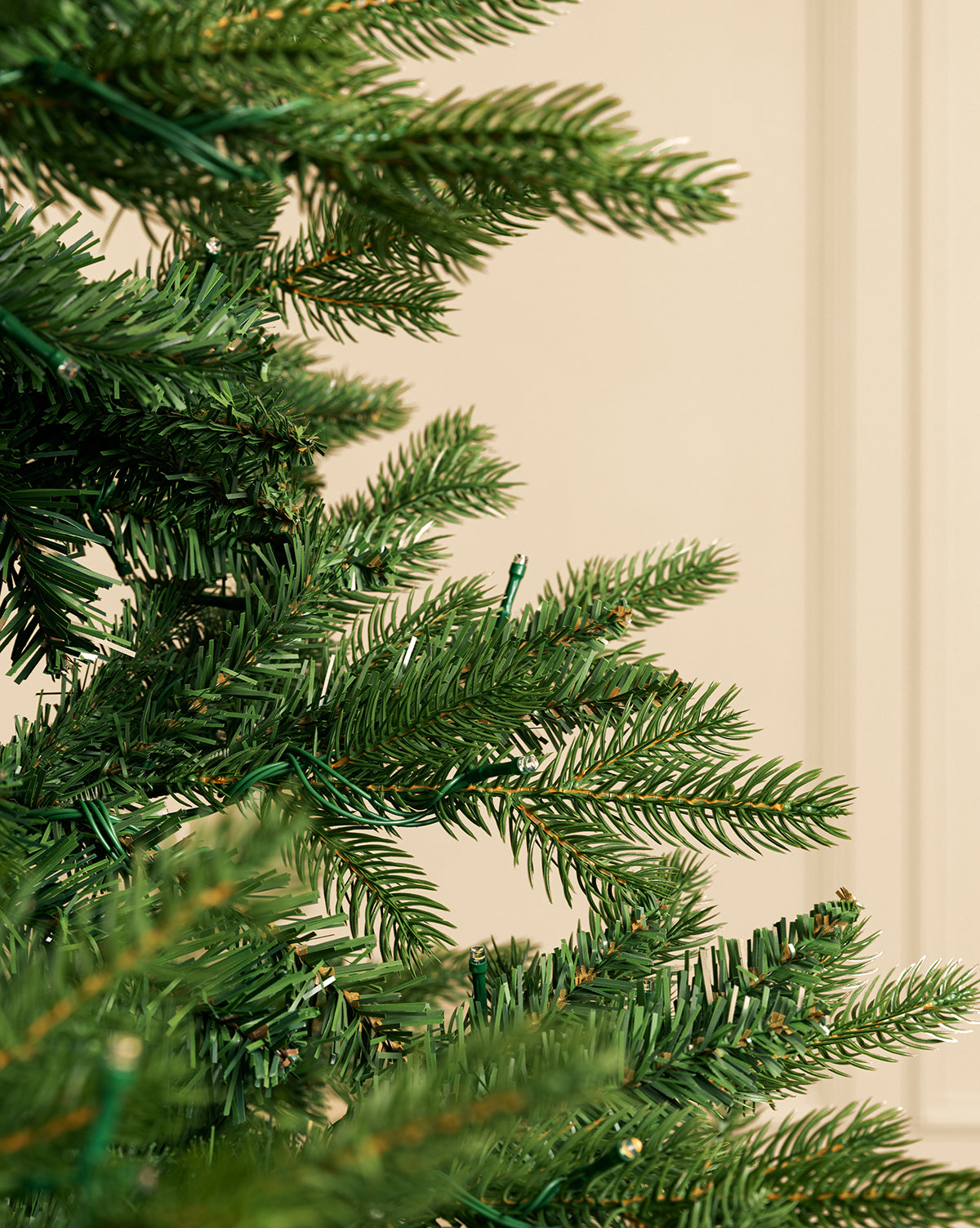 Close-up of realistic branches on a green 9' Allison Pine Pre-Lit Faux Tree set against a plain beige background, with the undecorated tree occupying the left side of the image, by Vendixs