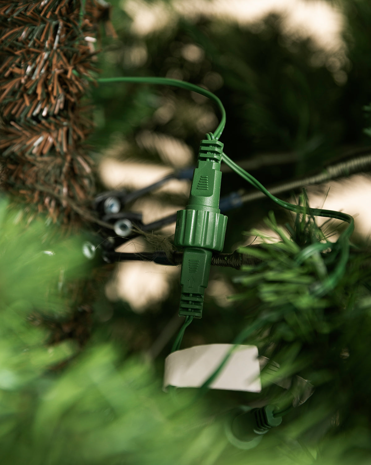 A close-up shows a green electrical connector plugged together among branches, part of the 9' Allison Pine Pre-Lit Faux Tree, by Vendixs