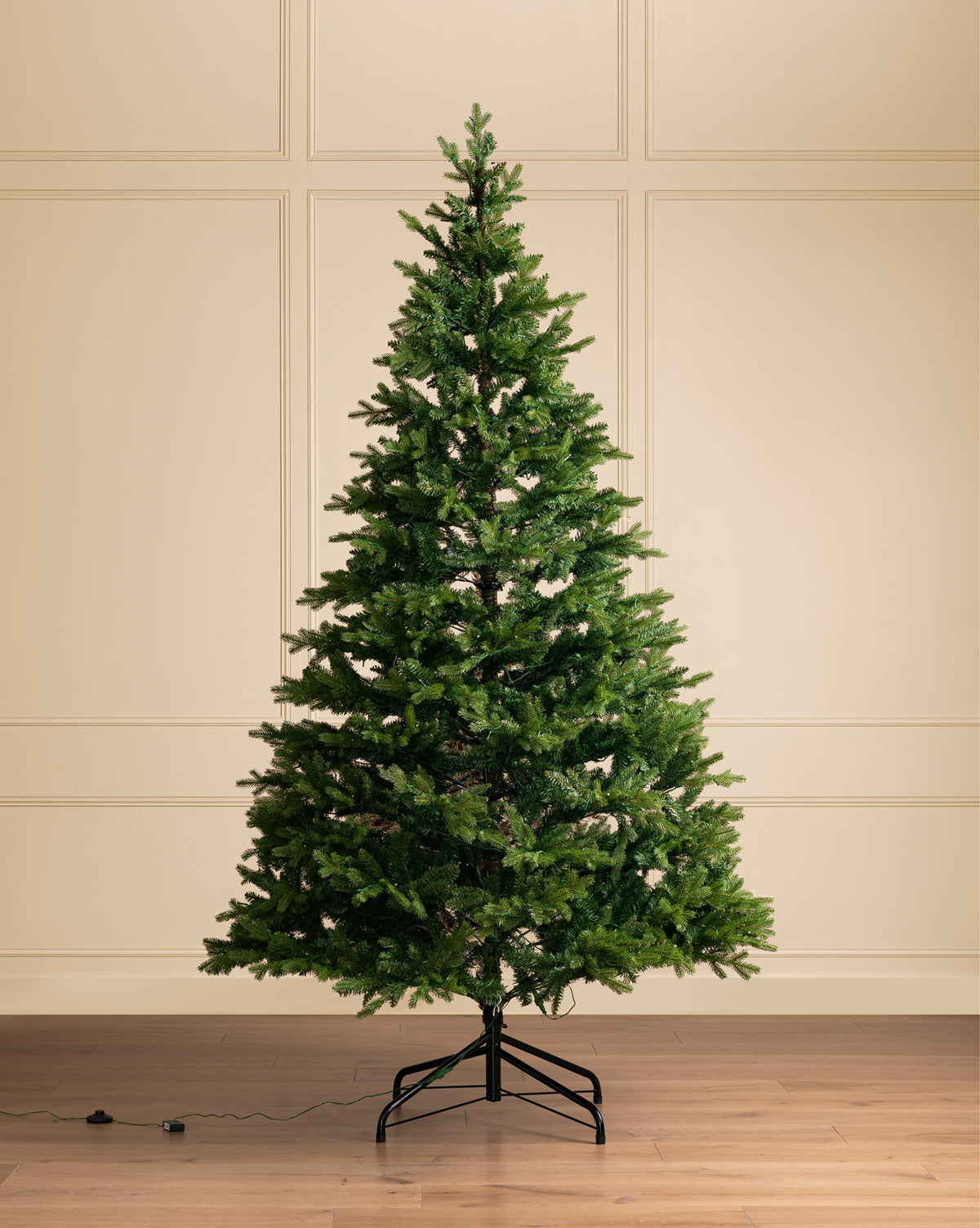 The 9' Allison Pine Pre-Lit Faux Tree, featuring dense, lifelike branches, stands undecorated on a metal stand in a room with light-paneled walls and hardwood floors. An electrical cord and foot pedal rest on the floor nearby, by McGee & Co.