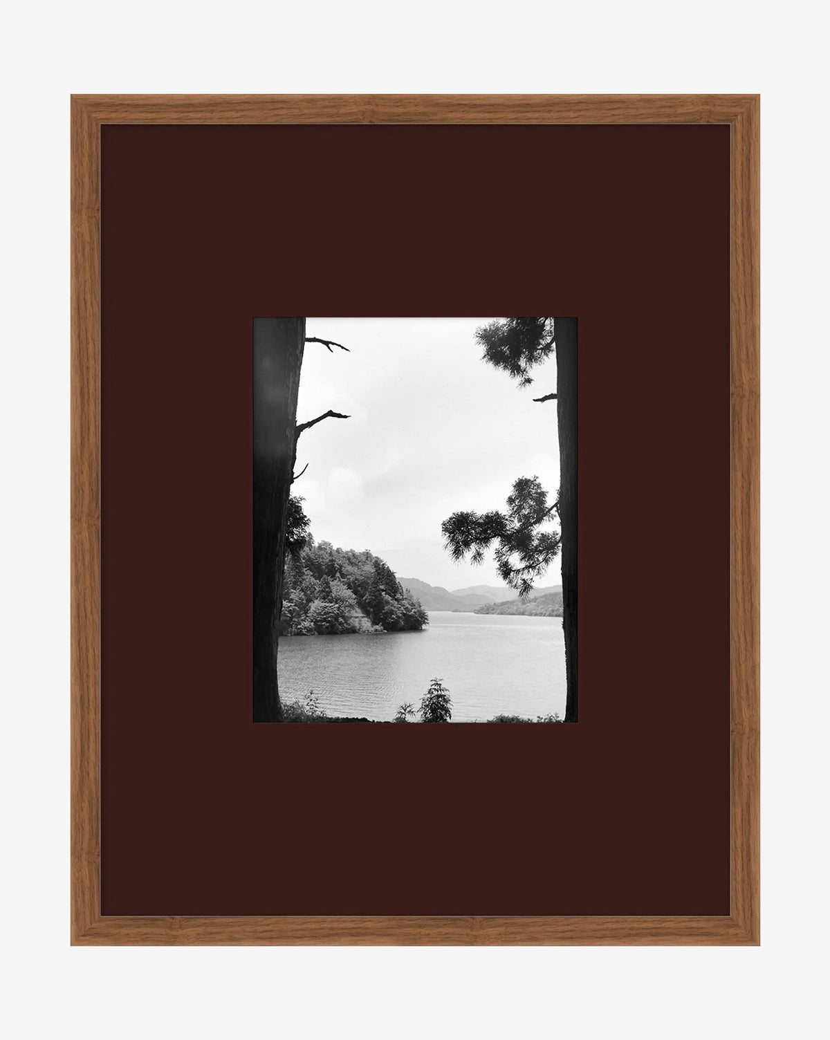 A Day in Lake Time III is a black-and-white giclée print depicting a tranquil lake with trees and distant hills, beautifully presented in a brown wooden frame with a dark mat—an elegant piece of lake wall art, by Vendixs