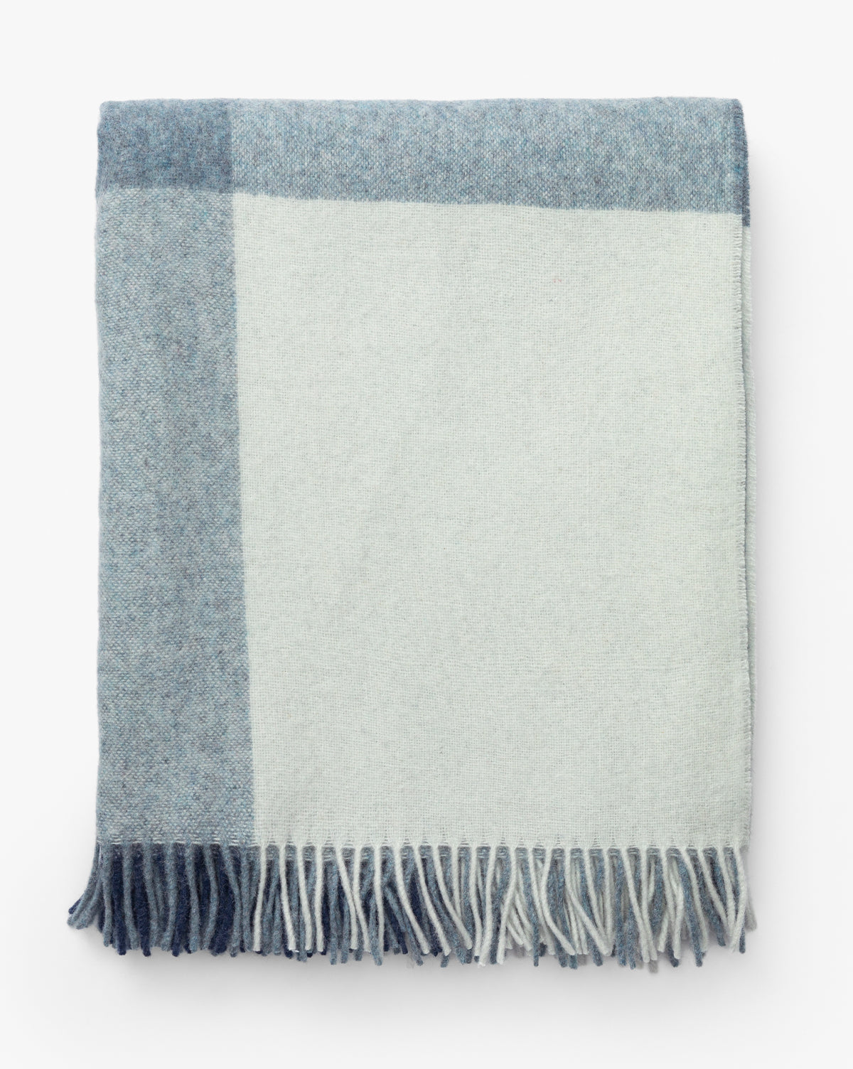 The Fibre Abner Throw is a folded, eco-friendly blanket with a simple block pattern in light blue and off-white, finished with fringe along the bottom edge. Vendixs
