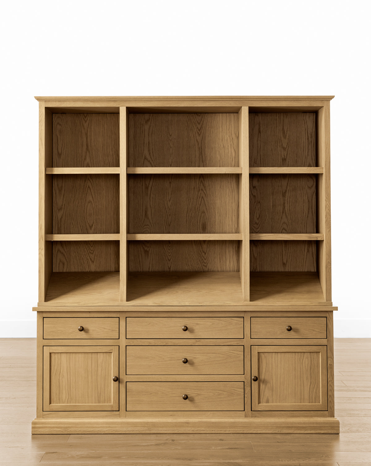 The Adler Oak Cabinet by BOUVRIE INTERNATIONAL VIET NAM CO., LTD. is a spacious wooden storage unit with three open shelves, six drawers, and two lower cabinets, shown on a light wood floor against a plain white background. Vendixs