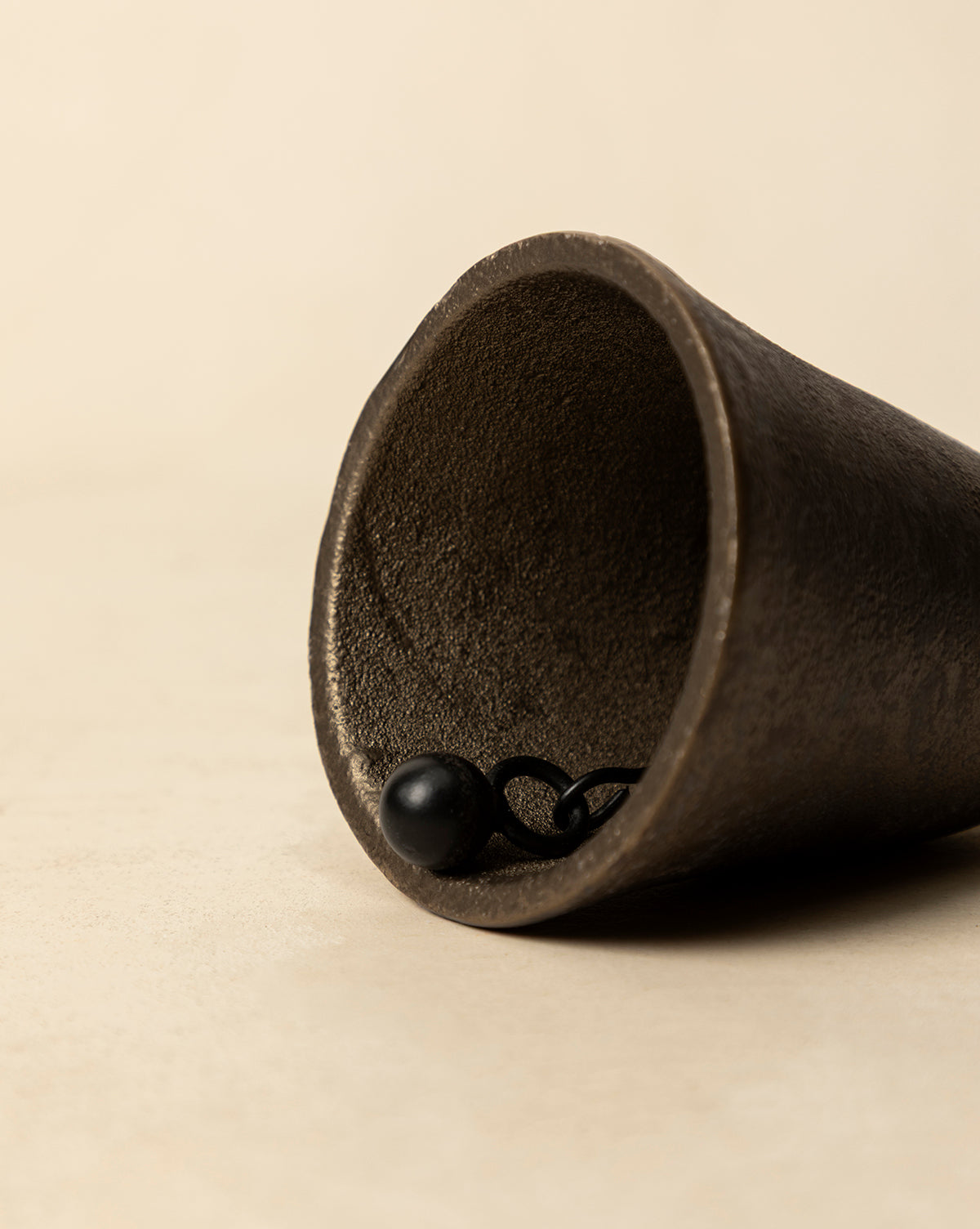 Aged Brass Bell lying on its side on a light beige surface reveals the inside and clapper, capturing vintage charm ideal for holiday decor, by Vendixs