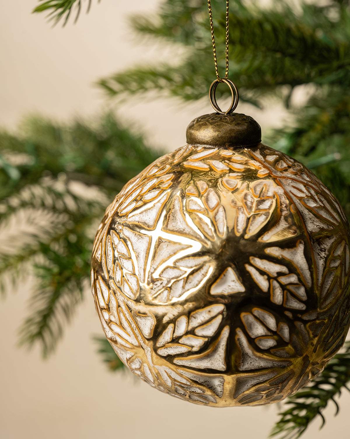 The Alessandro Glass Ornament features a gold leaf and snowflake design, shown in close-up as it hangs from a green Christmas tree branch for festive holiday decor, by Vendixs