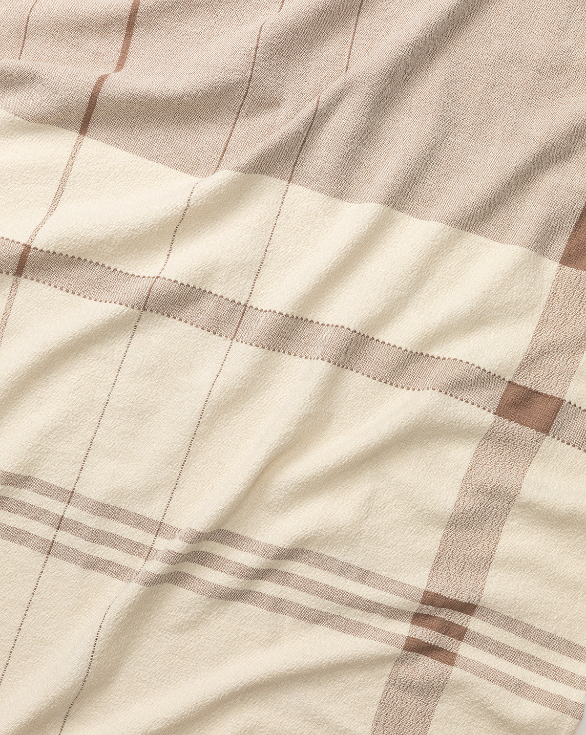 A close-up of the ILA HOME FASHIONS Alex Plaid Throw highlights its soft texture and gentle wrinkles in neutral beige, cream, and thin brown stripes—an inviting, luxurious throw blanket for any space. Vendixs