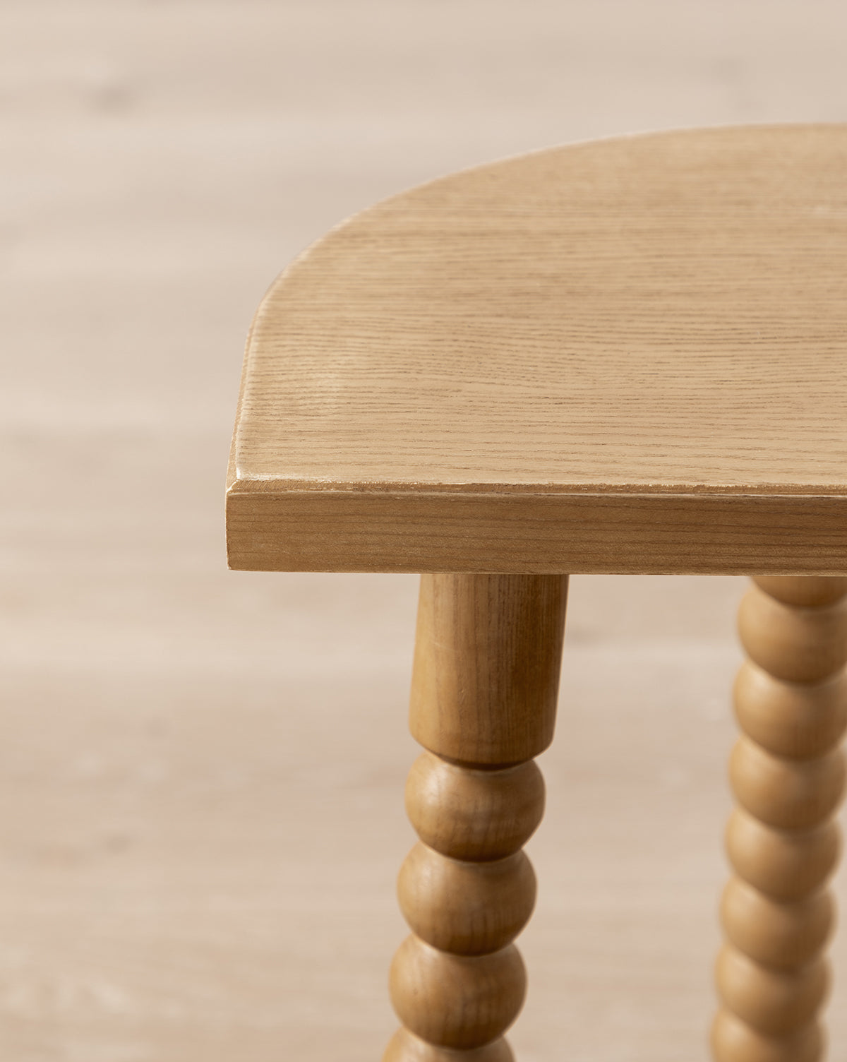 Close-up of the Makerspalm Alice Honey Wood Stool, featuring a rounded edge, spindle-style legs, and a light natural finish that highlights its craftsmanship, adding timeless charm to any space. Vendixs