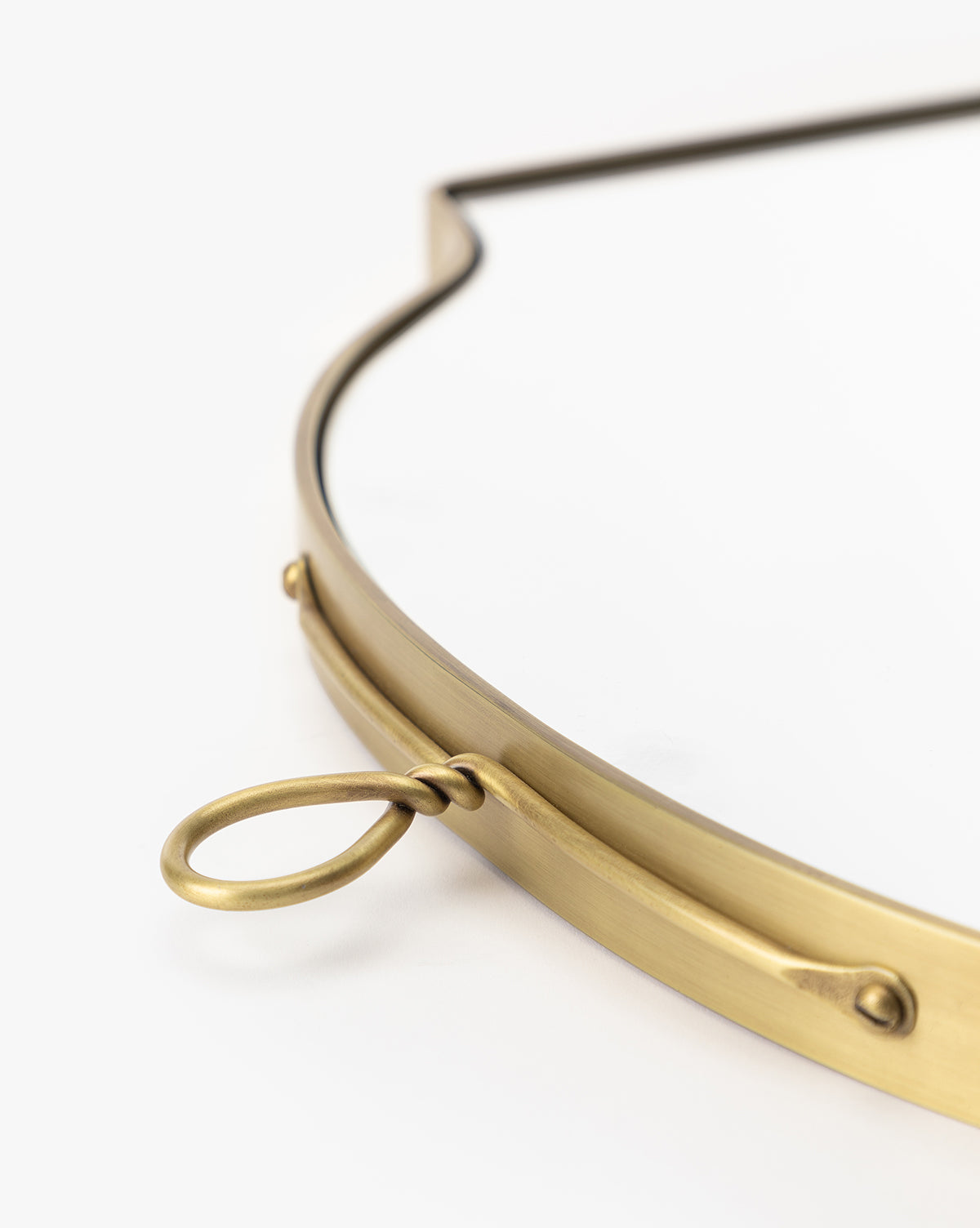 Close-up of the Allegheny Wall Mirror, featuring a gold-colored metal frame, curved edge, and oval hanging loop, set against a white background by Vendixs