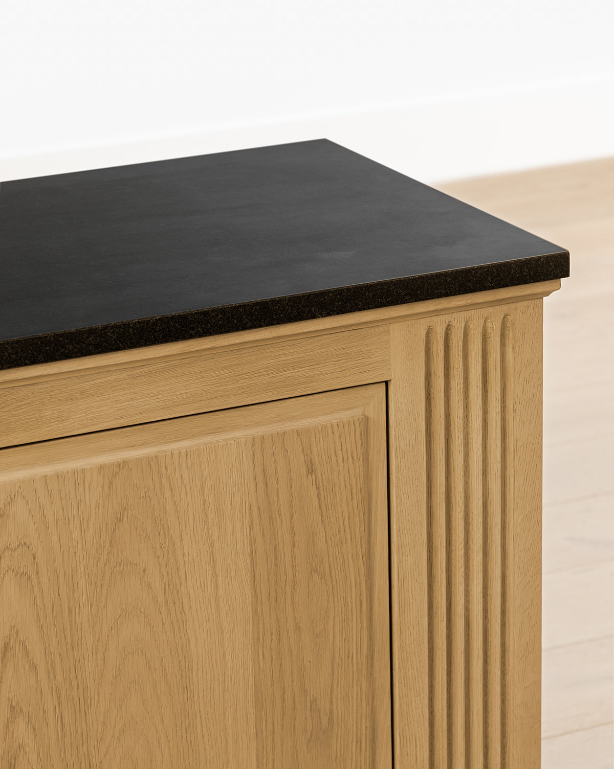 A close-up of the Ambrose Sideboard featuring fluted detailing and a flat black countertop, set against a light-colored wall and floor, by Vendixs
