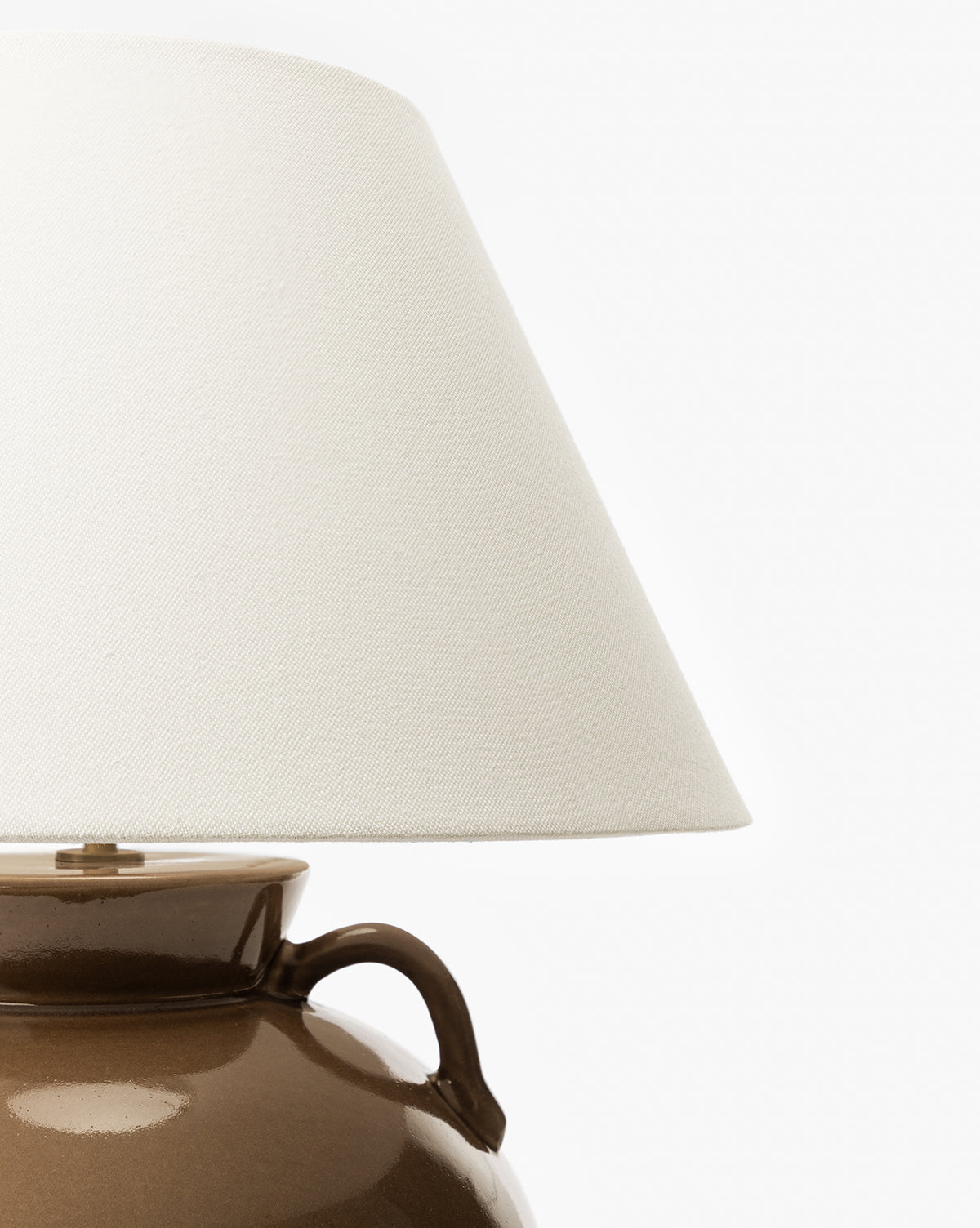 A close-up of the Amphora Table Lamp highlights its brown ceramic base and white fabric shade, with only the upper part of the lamp and lower portion of the shade visible against a plain white background, by Vendixs
