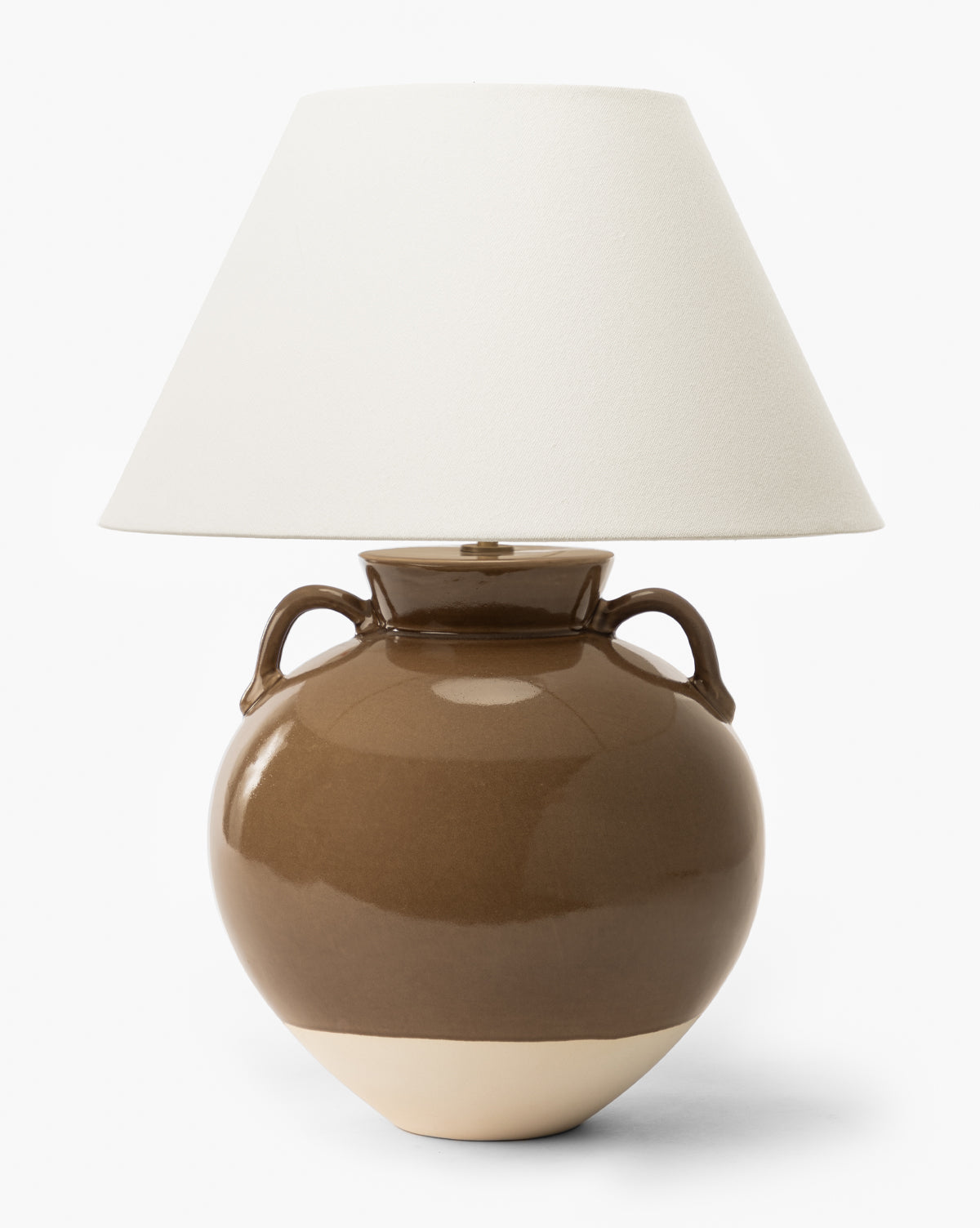 The Makerspalm Amphora Table Lamp features a glossy brown ceramic base with two side handles and a lighter bottom, topped with a wide off-white shade for a classic look. Vendixs