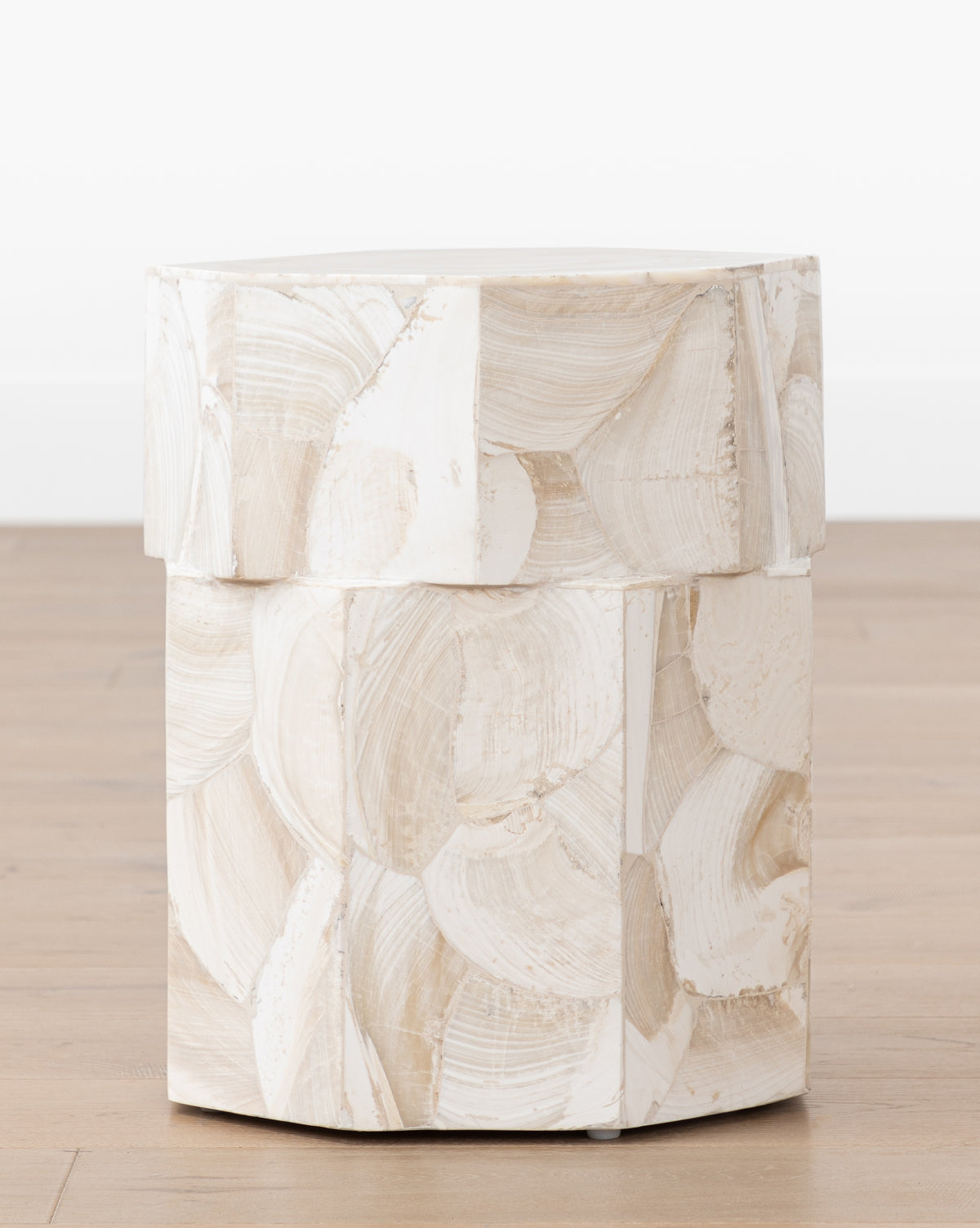 The Andrade Side Table by JANICE MINOR EXPORT, INC. features a round, contemporary design with textured beige and white brushstroke patterns, displayed on a wooden floor against a plain white background by Vendixs