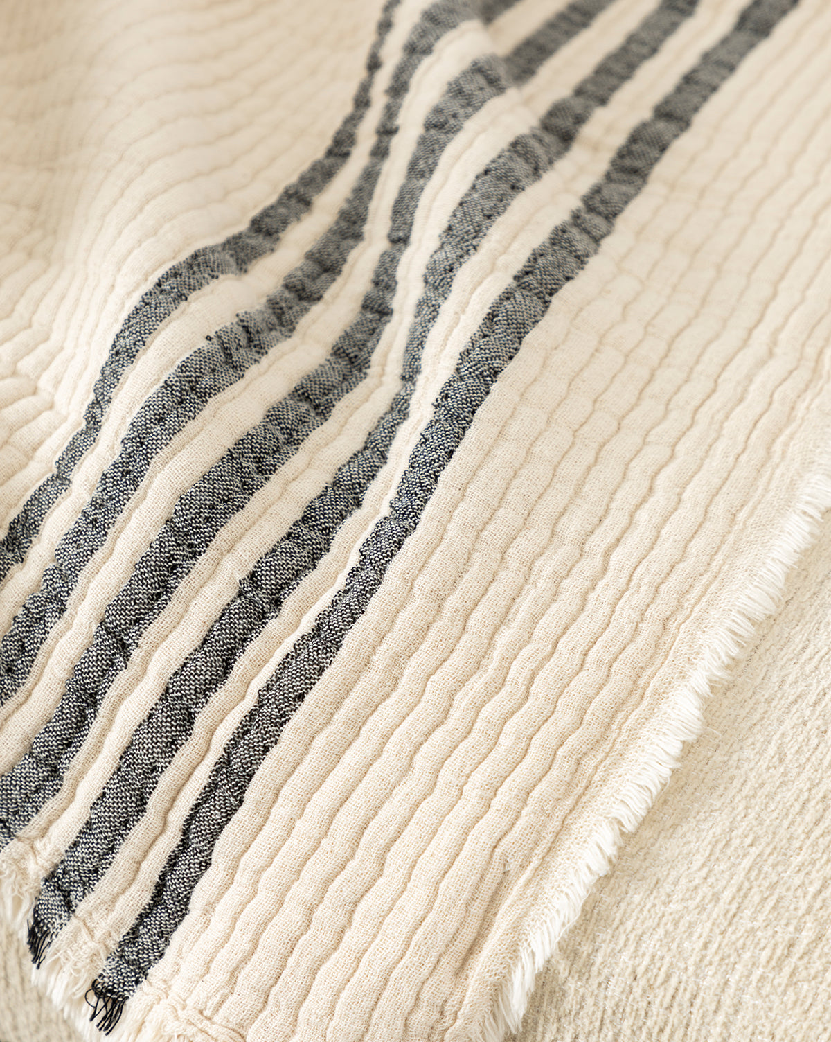 The Anneliese Striped Throw by Creative Co-op features cream-colored, textured cotton with three black stripes, a wavy quilted look, and slightly frayed edges—ideal for adding a luxurious accent to your home decor. Vendixs