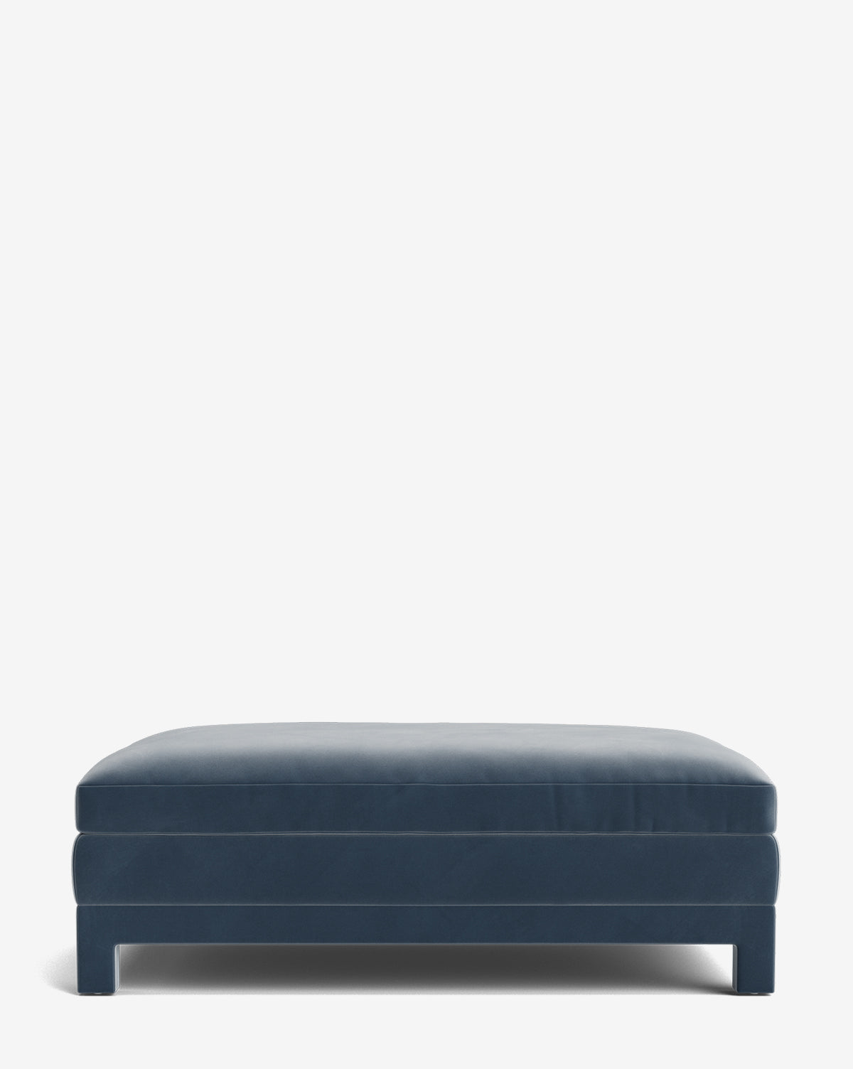 The Appoline Ottoman is a rectangular, modern piece with clean lines, dark blue upholstery, and short block legs, shown against a plain white background by McGee & Co.