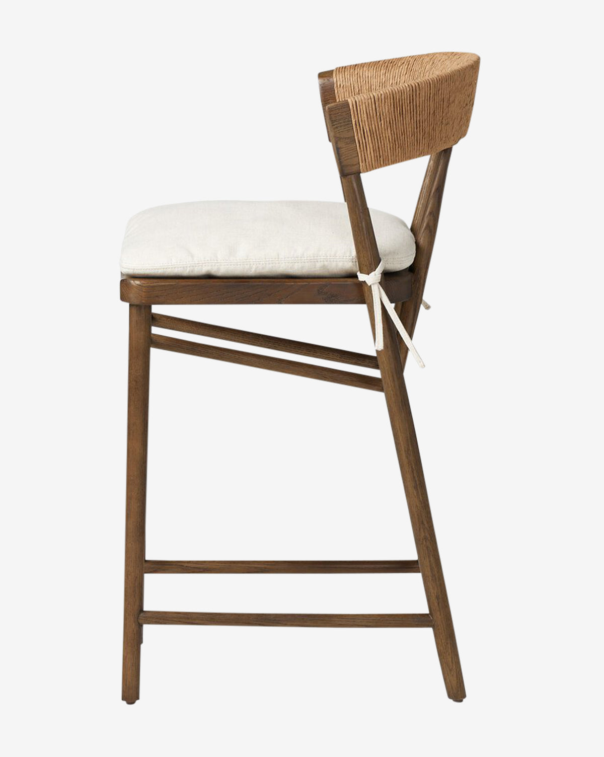 Side view of the Four Hands Ardent Stool, featuring a solid oak frame with angled legs, woven rope backrest, and a light cushioned seat secured with fabric ties—ideal for your kitchen bar. Vendixs